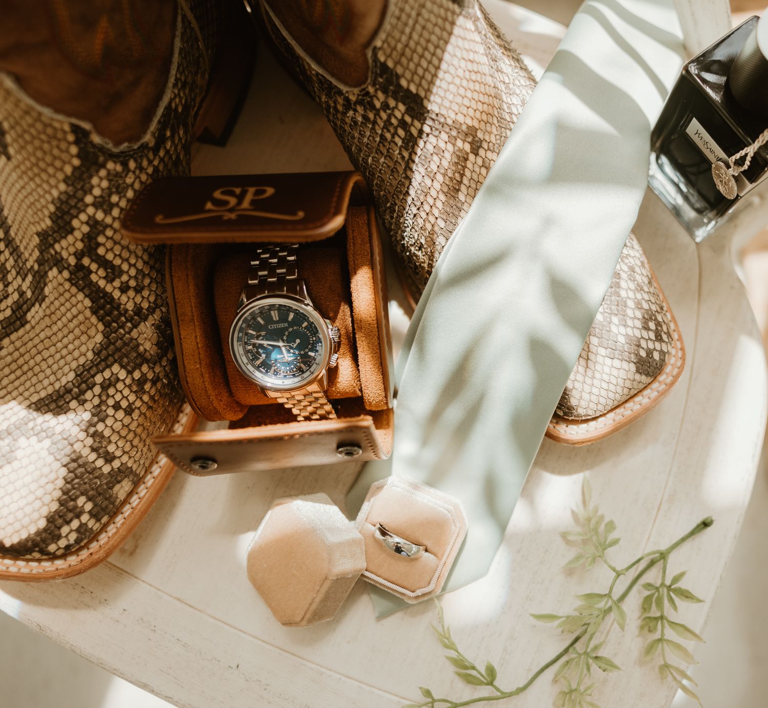 Wedding details featuring a luxurious wooden watch box next to snakeskin boots and delicate accessories.