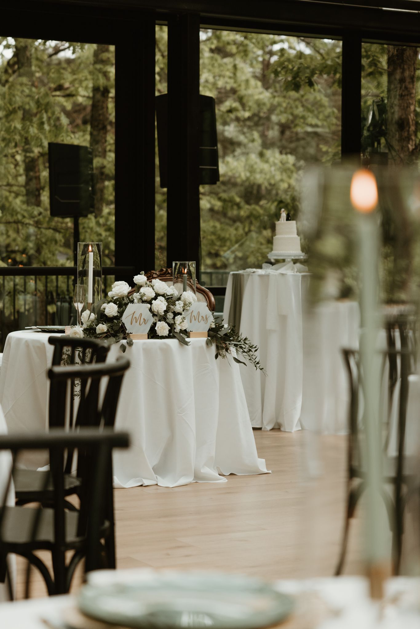 An elegant wedding reception setup with white tablecloths, floral centerpieces and a cake table under a covered patio.