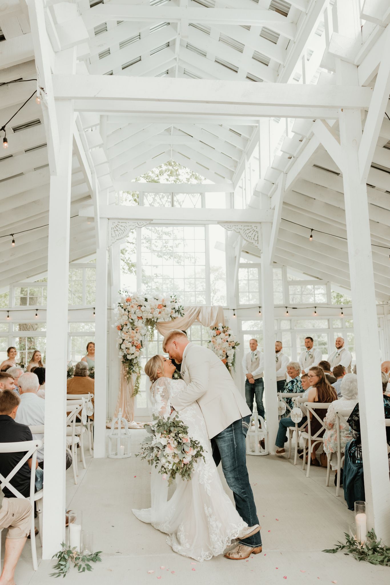 Wedding ceremony in a bright white chapel with vaulted ceilings and romantic floral decorations.