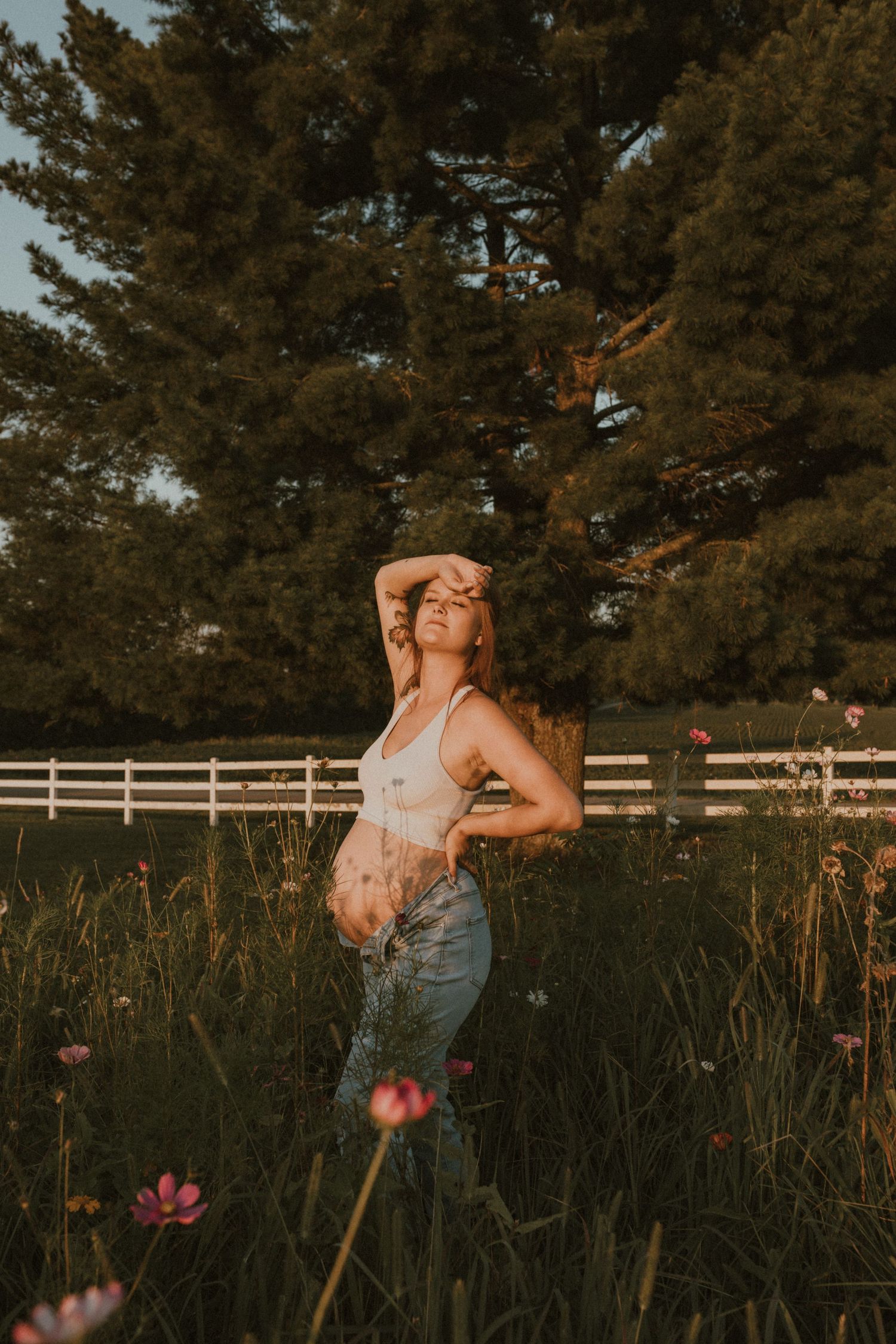 Someone poses in a field of wildflowers during golden hour with a white fence in the distance.