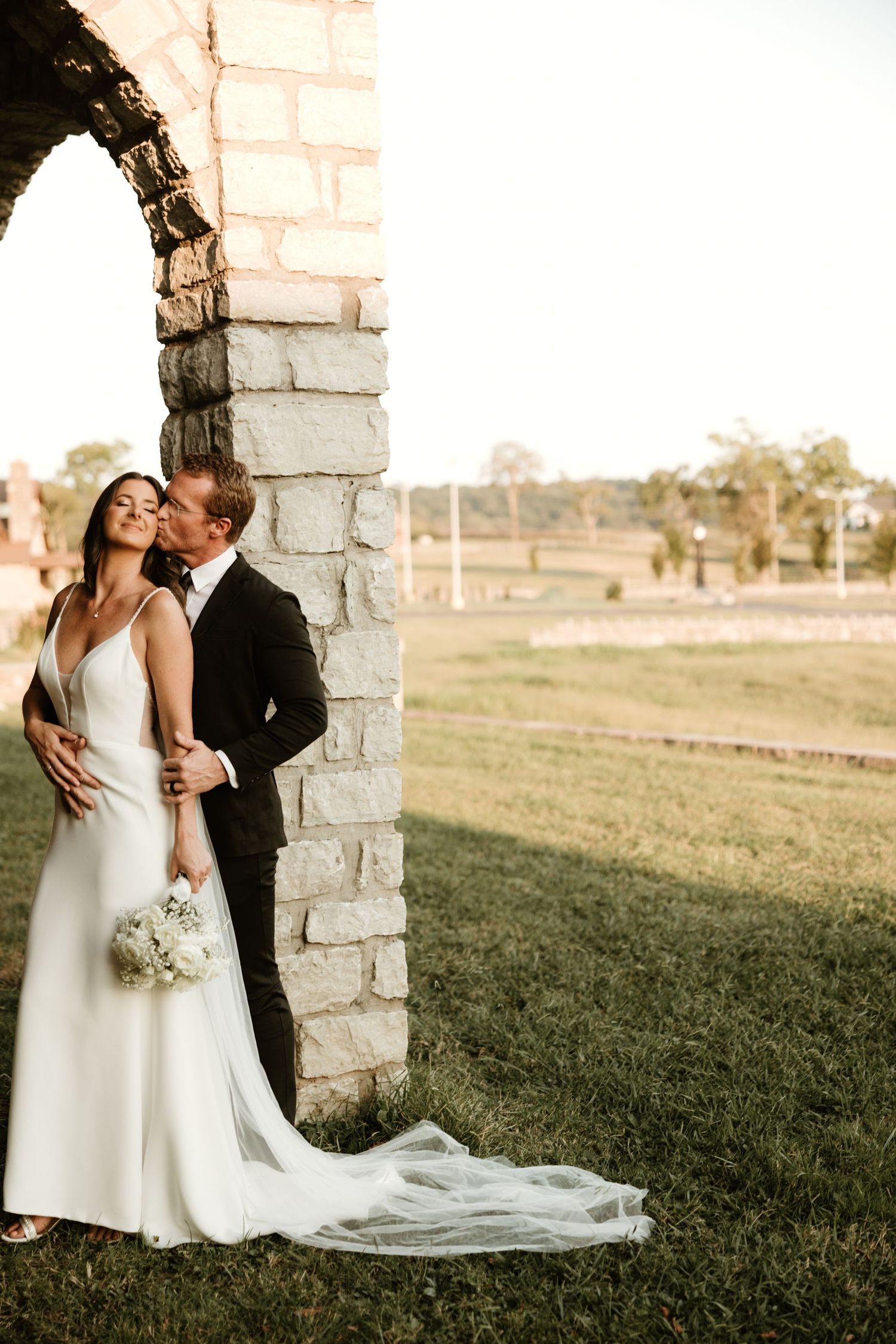 Romantic wedding moment captured under a stone archway at golden hour.