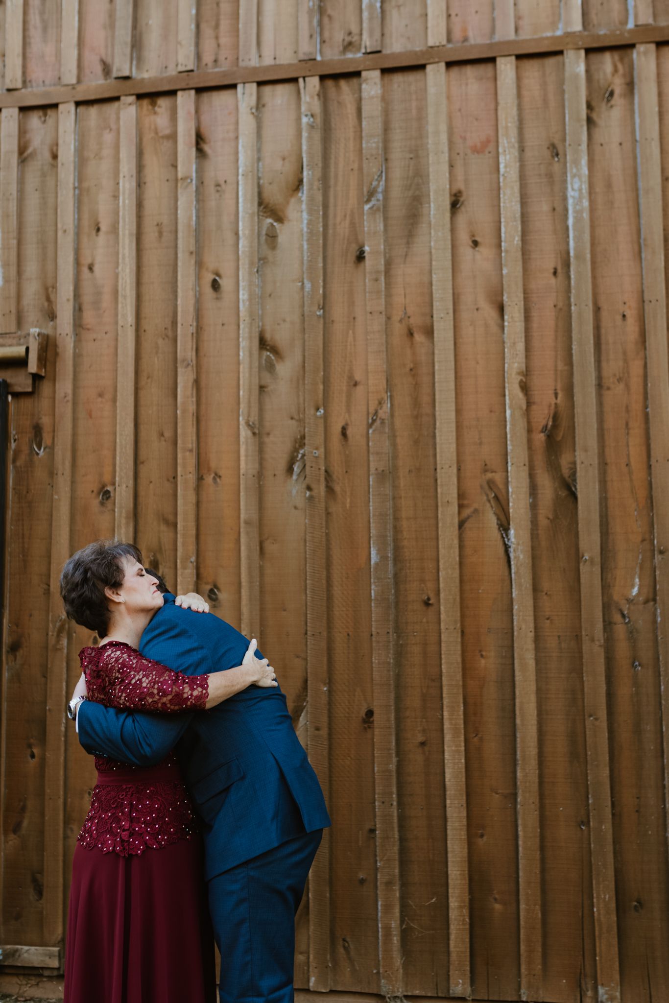 A romantic couple embraces in front of a rustic wooden fence during a photoshoot.