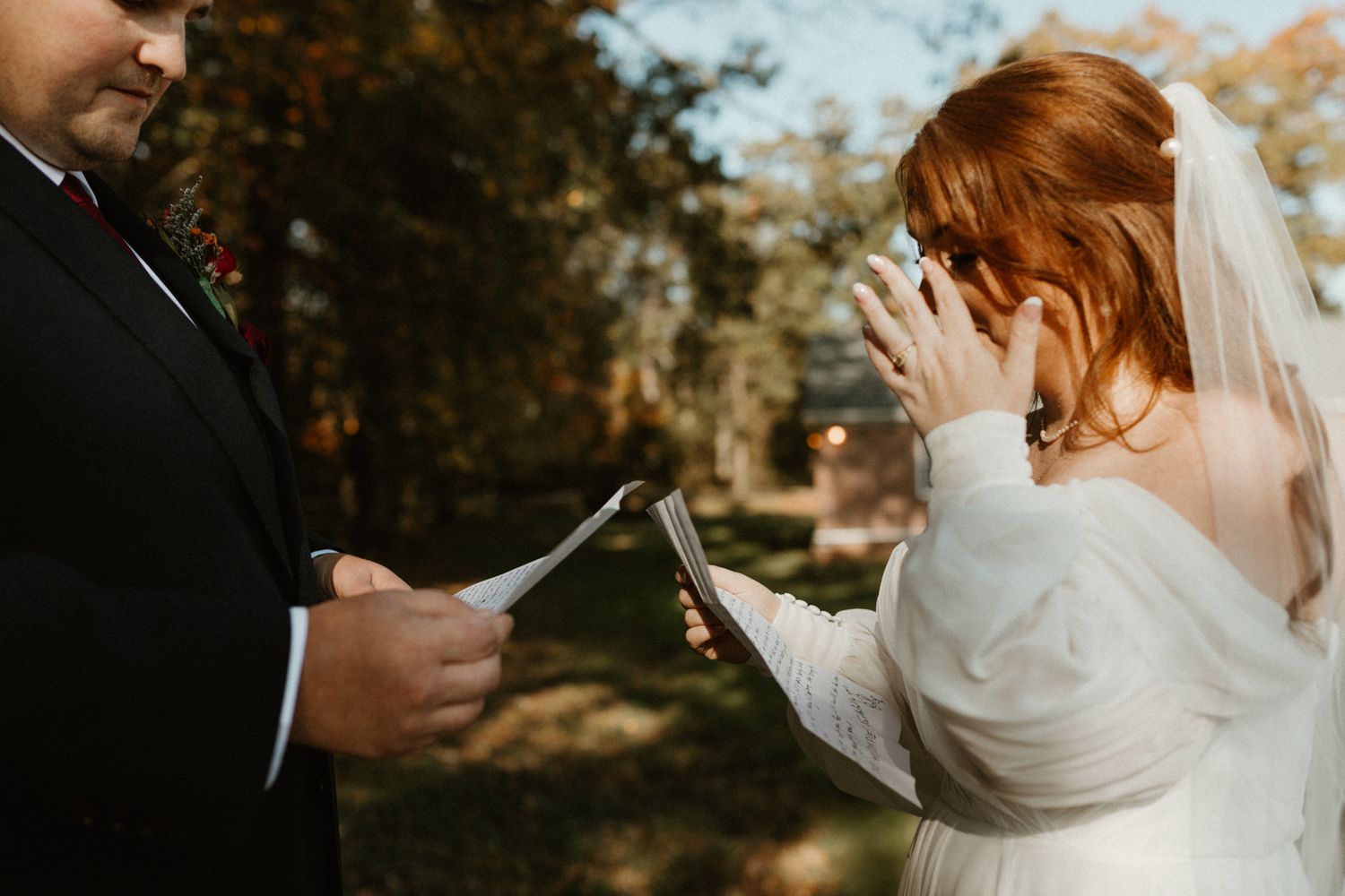 Emotional wedding ceremony moment in autumn sunshine as couple exchanges vows outdoors in garden setting.