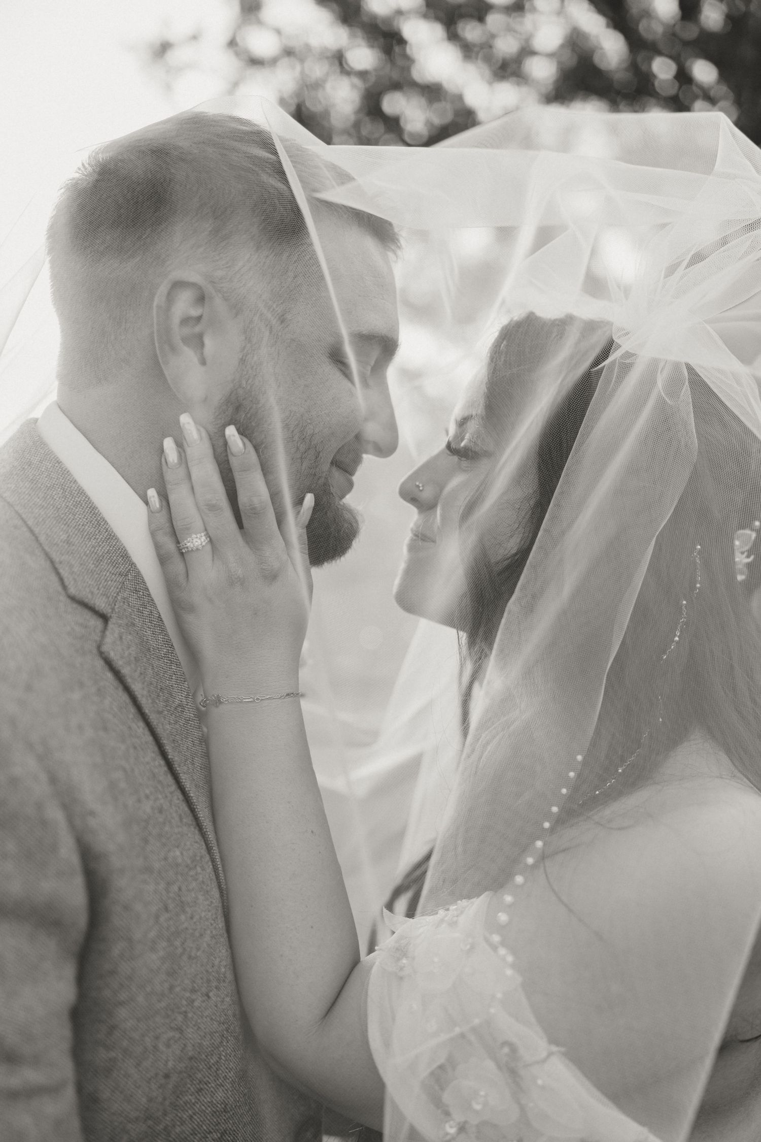 A tender moment between newlyweds as they embrace under a wedding veil in black and white photography.