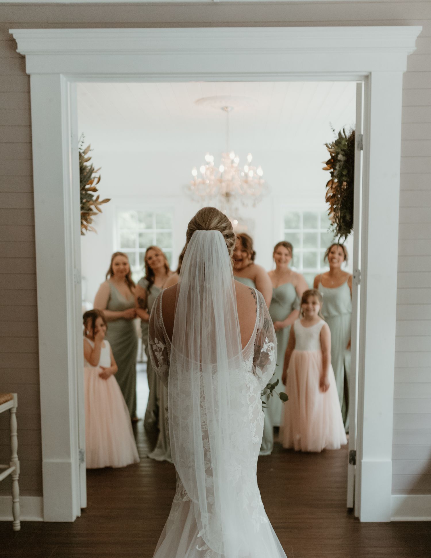 Wedding party in pastel dresses gathering behind an elegant white doorframe.