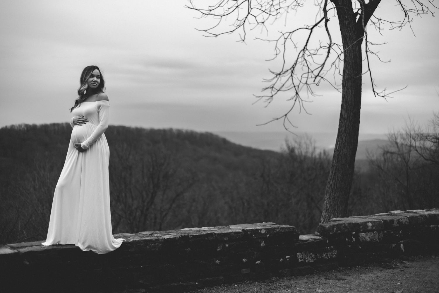 A silhouetted figure in a flowing white dress stands on a stone wall against a misty mountain landscape.