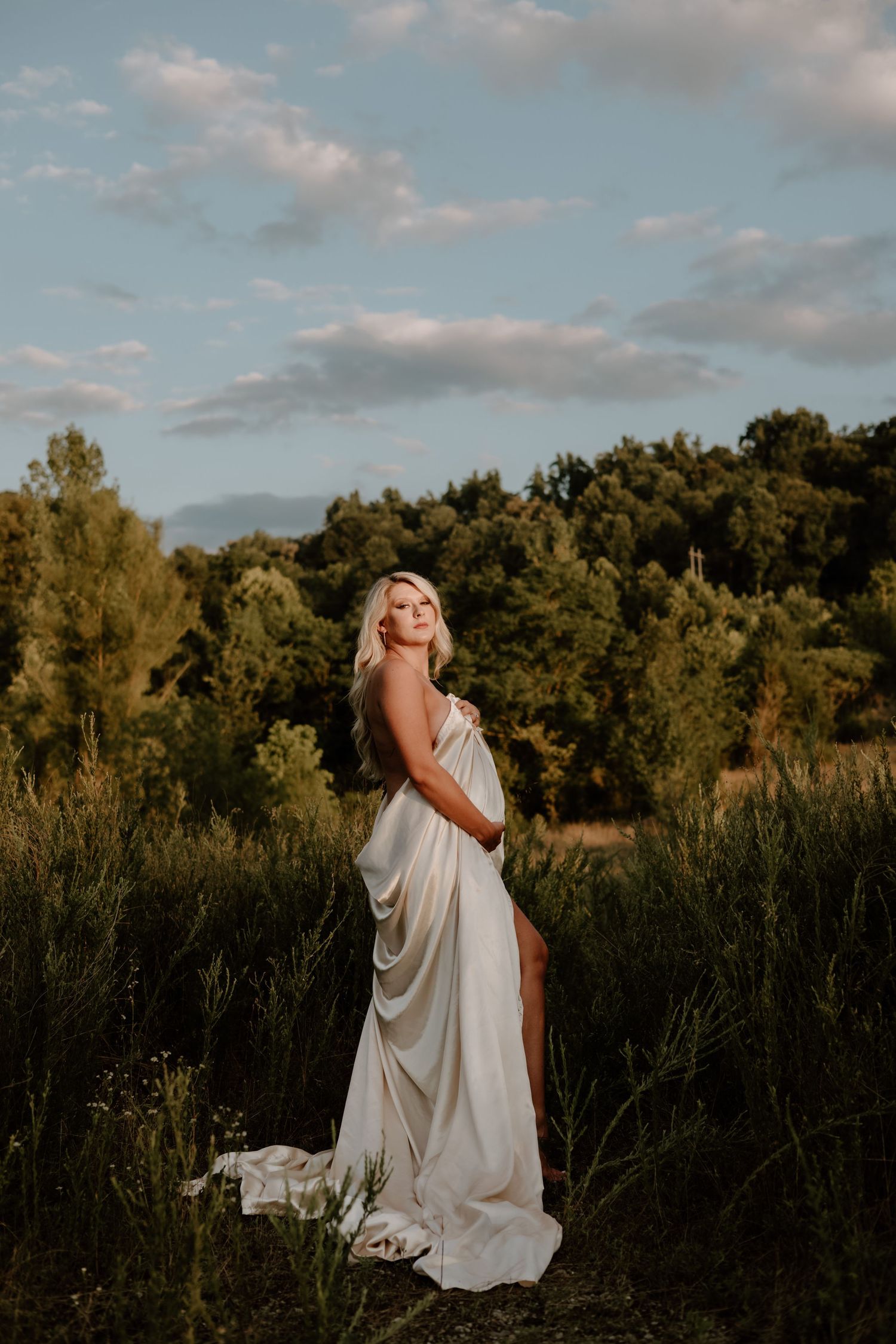 Ethereal outdoor photography with flowing white dress against sunset sky and trees.