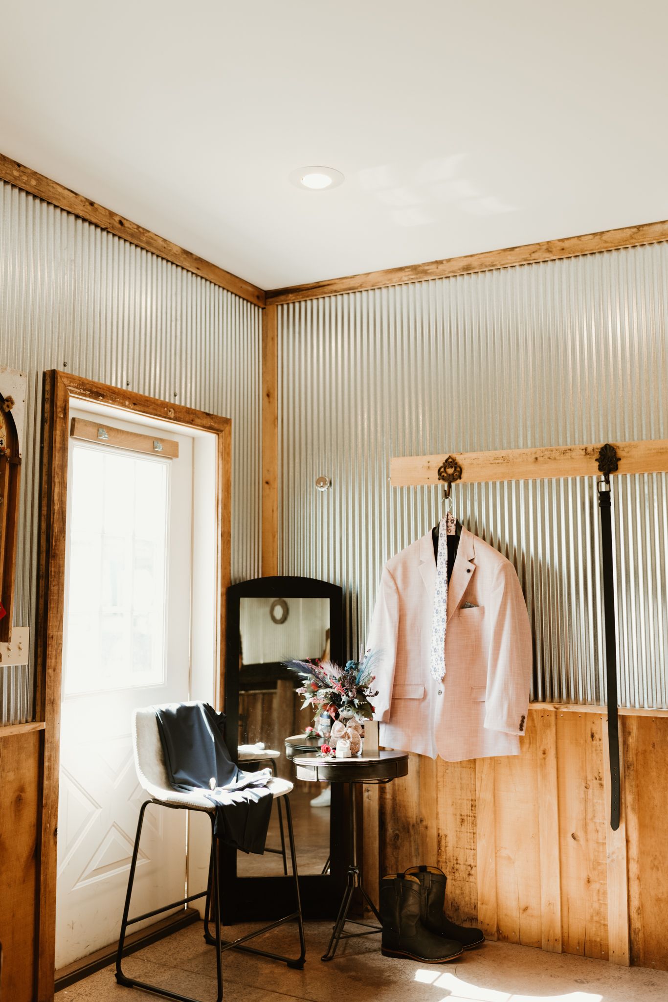 A light pink suit jacket hangs next to a vintage TV in a rustic room with corrugated metal walls and wood trim.