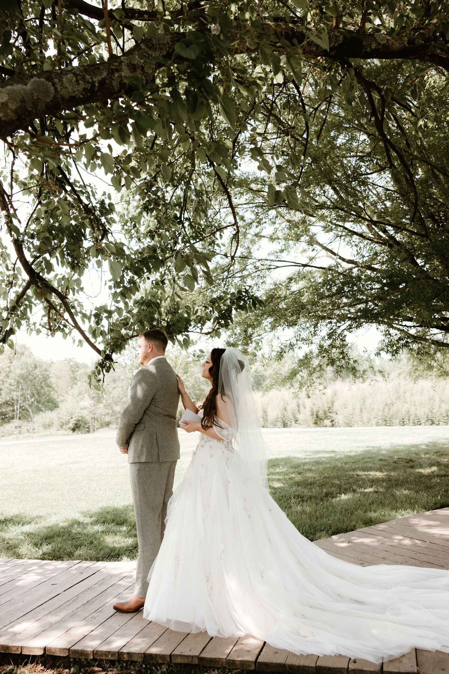 A bride and groom share an intimate moment on a wooden deck surrounded by trees in an outdoor setting.