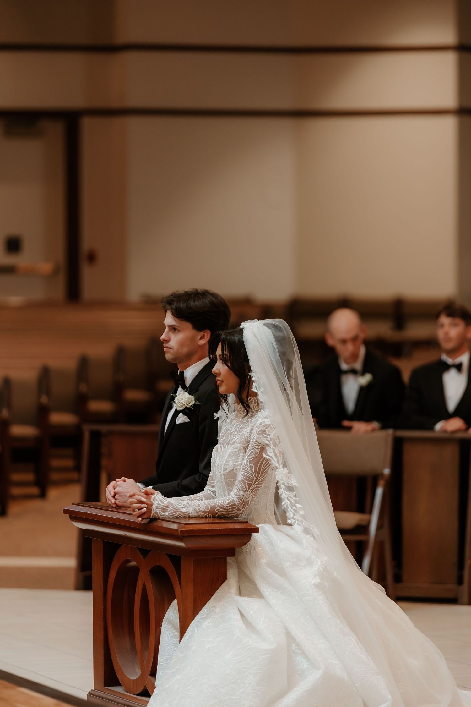 Bride and groom kneeling at altar during church wedding ceremony, bride in lace gown with veil.