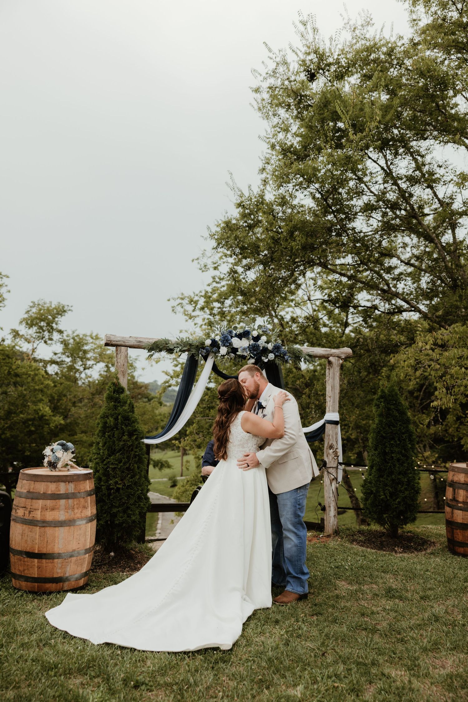 Wedding celebration in rustic outdoor venue with wooden barrel decor and green trees.