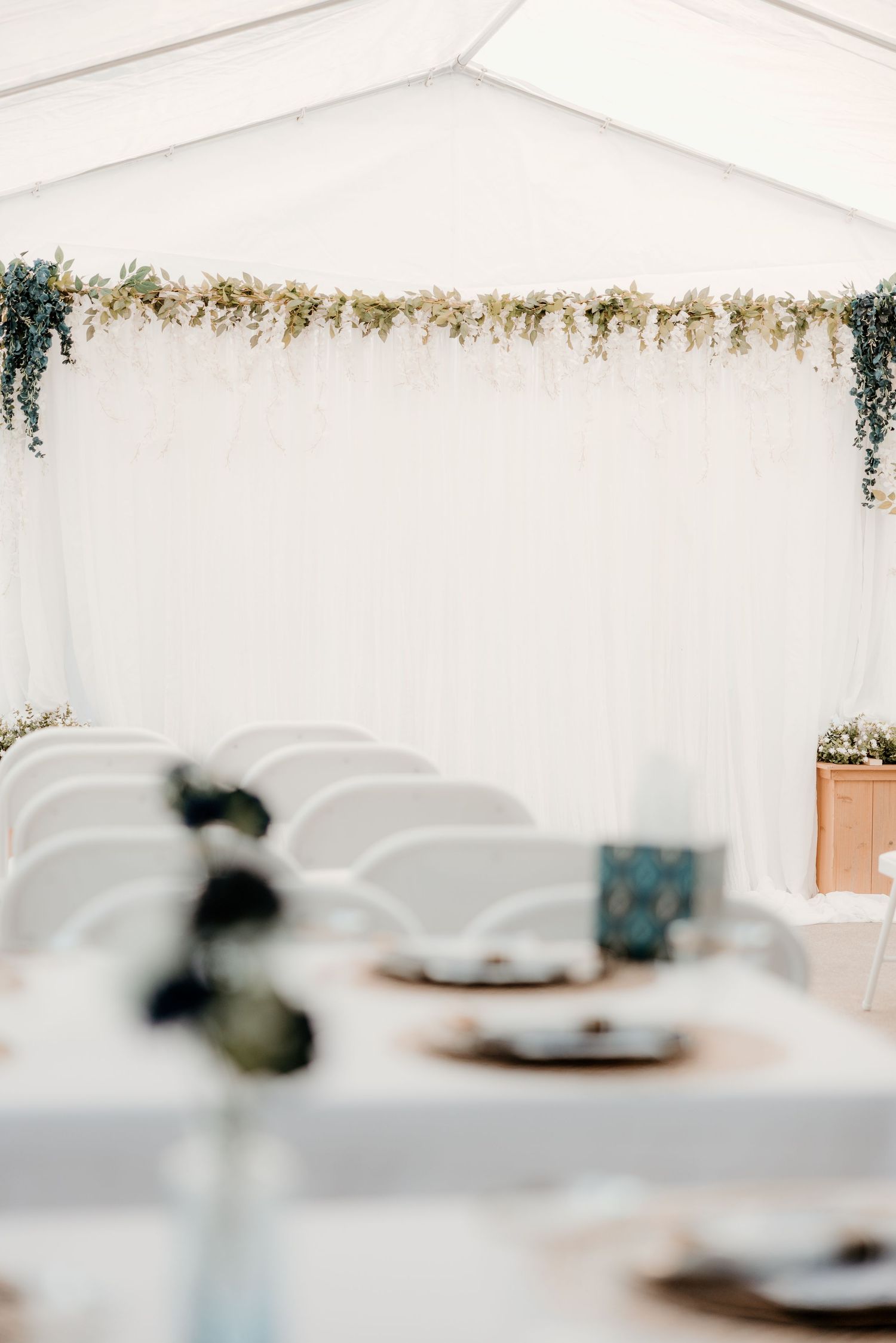 Elegant wedding reception tent with floral garland, white draping, and decorated tables with greenery centerpieces.