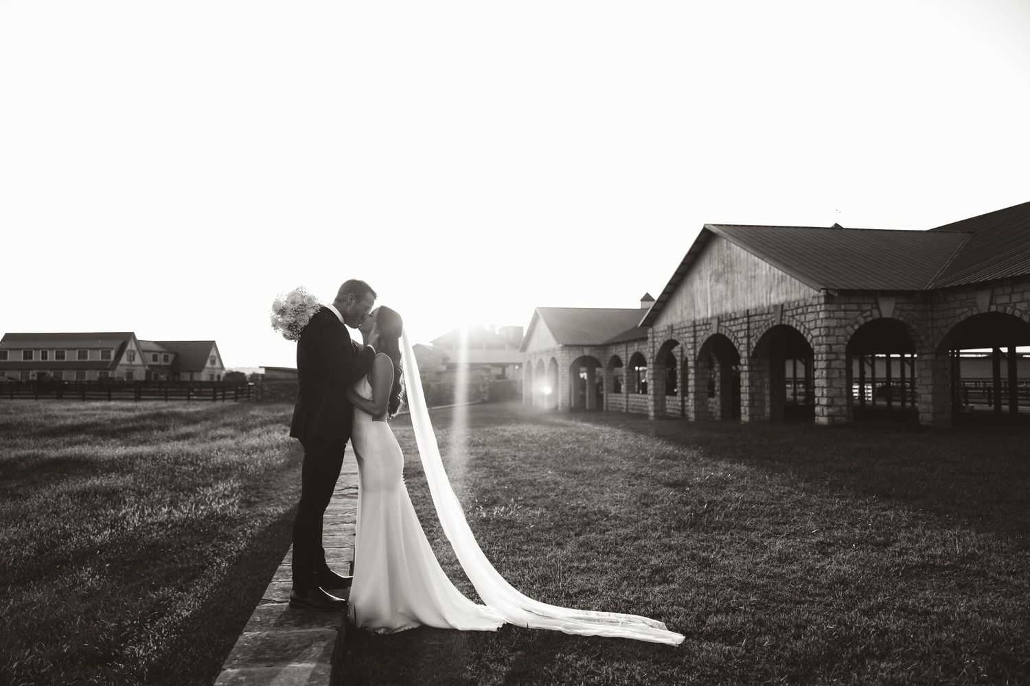A romantic silhouette photo of a couple in wedding attire during sunset with buildings in the background.