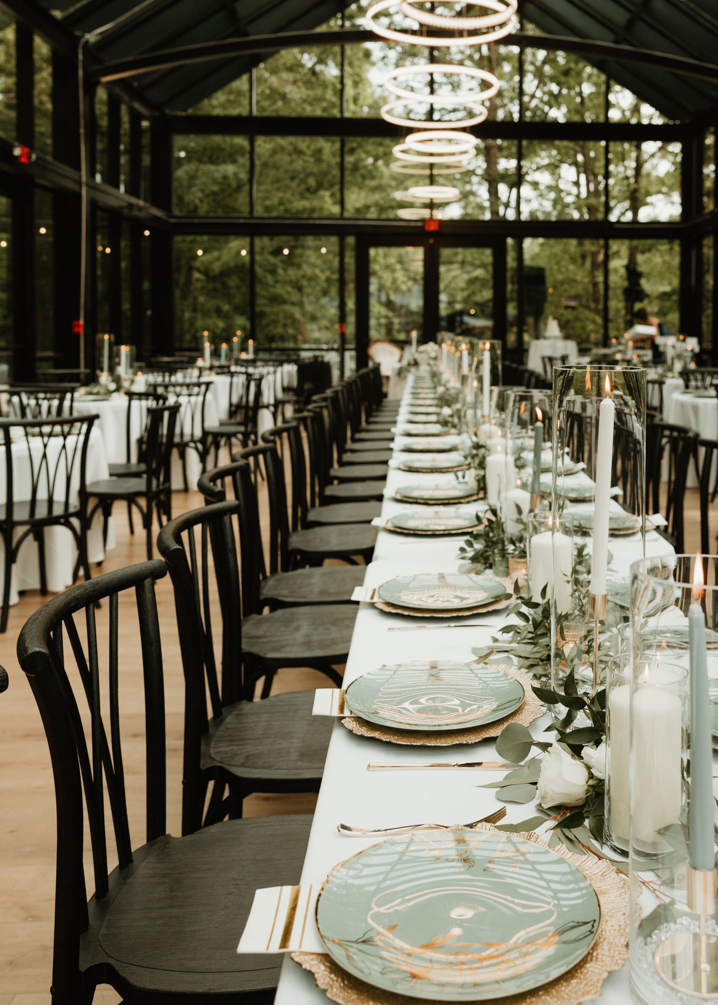 Elegant table settings with gold chargers and crystal glassware in a glass-enclosed reception venue.