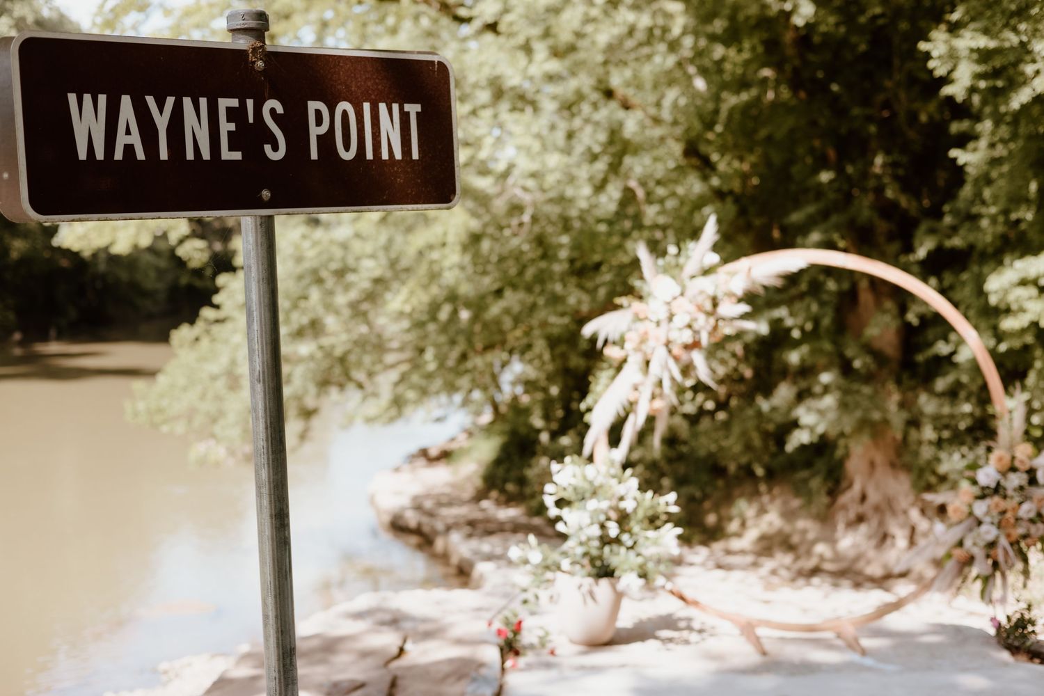 Street sign reading 'Wayne's Point' on a pole against a blurry natural background with foliage.