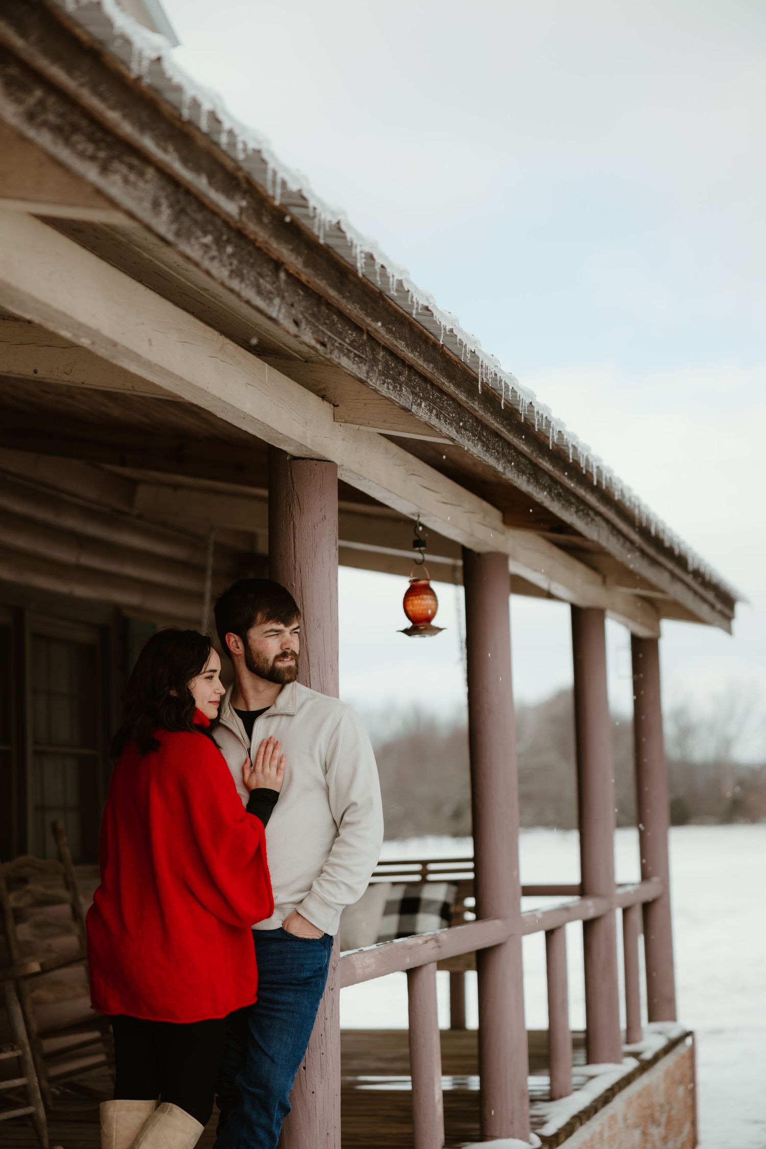 A romantic moment shared on a rustic covered porch during winter with a red sweater against white snow.