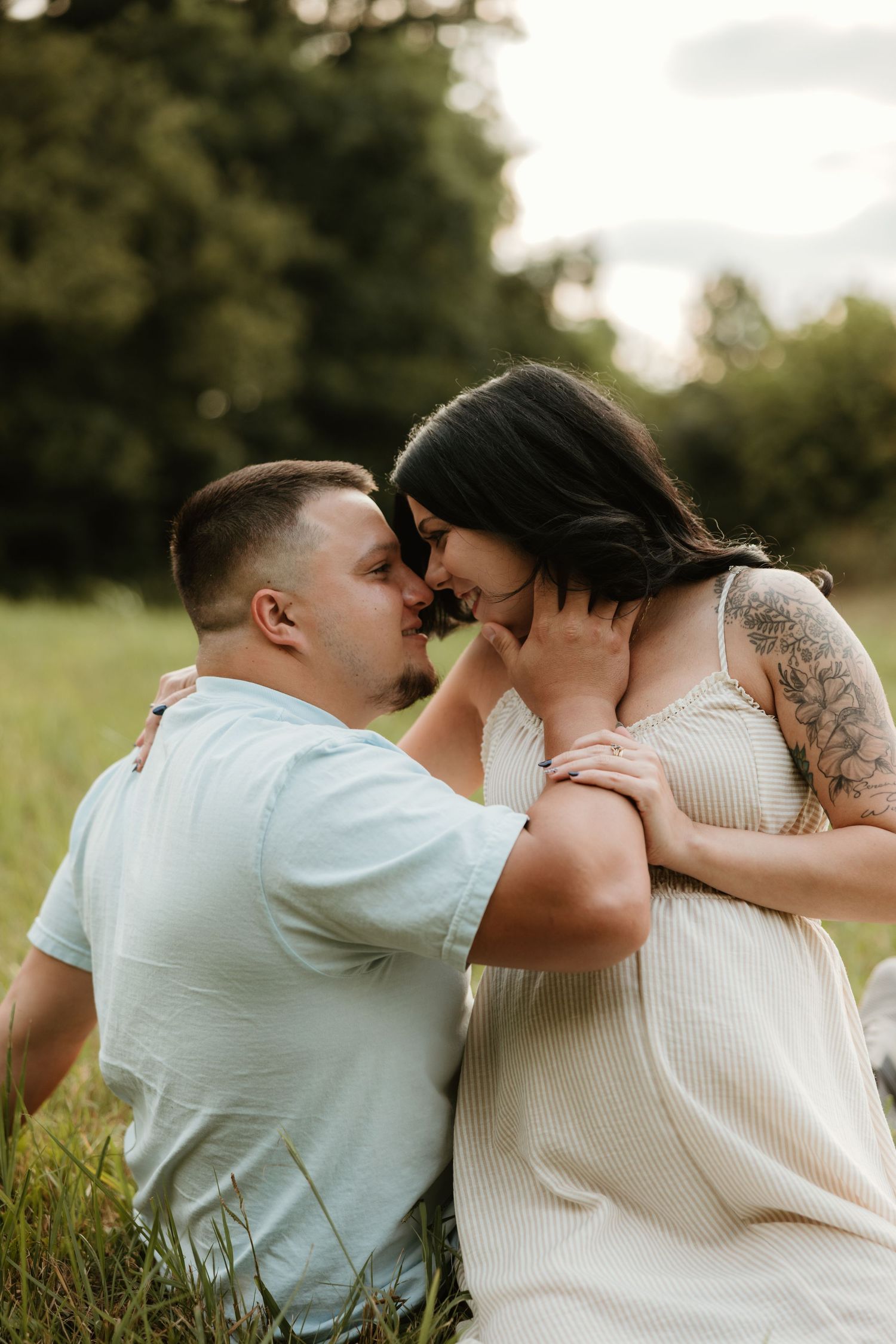 Intimate couple shares a tender moment while sitting together in a grassy field at sunset.