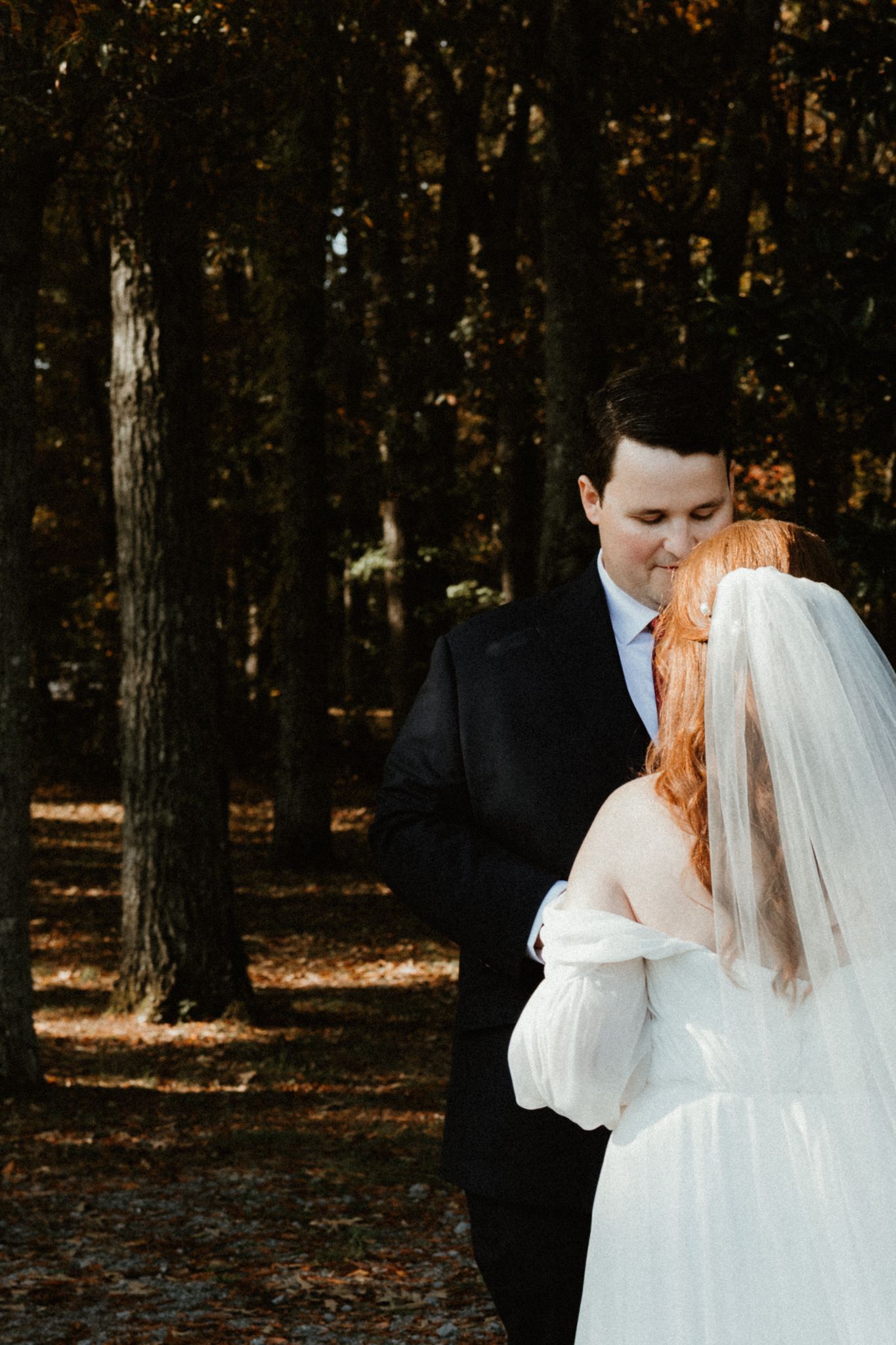A romantic outdoor autumn wedding photo shoot with a couple embracing among tall trees and fallen leaves.