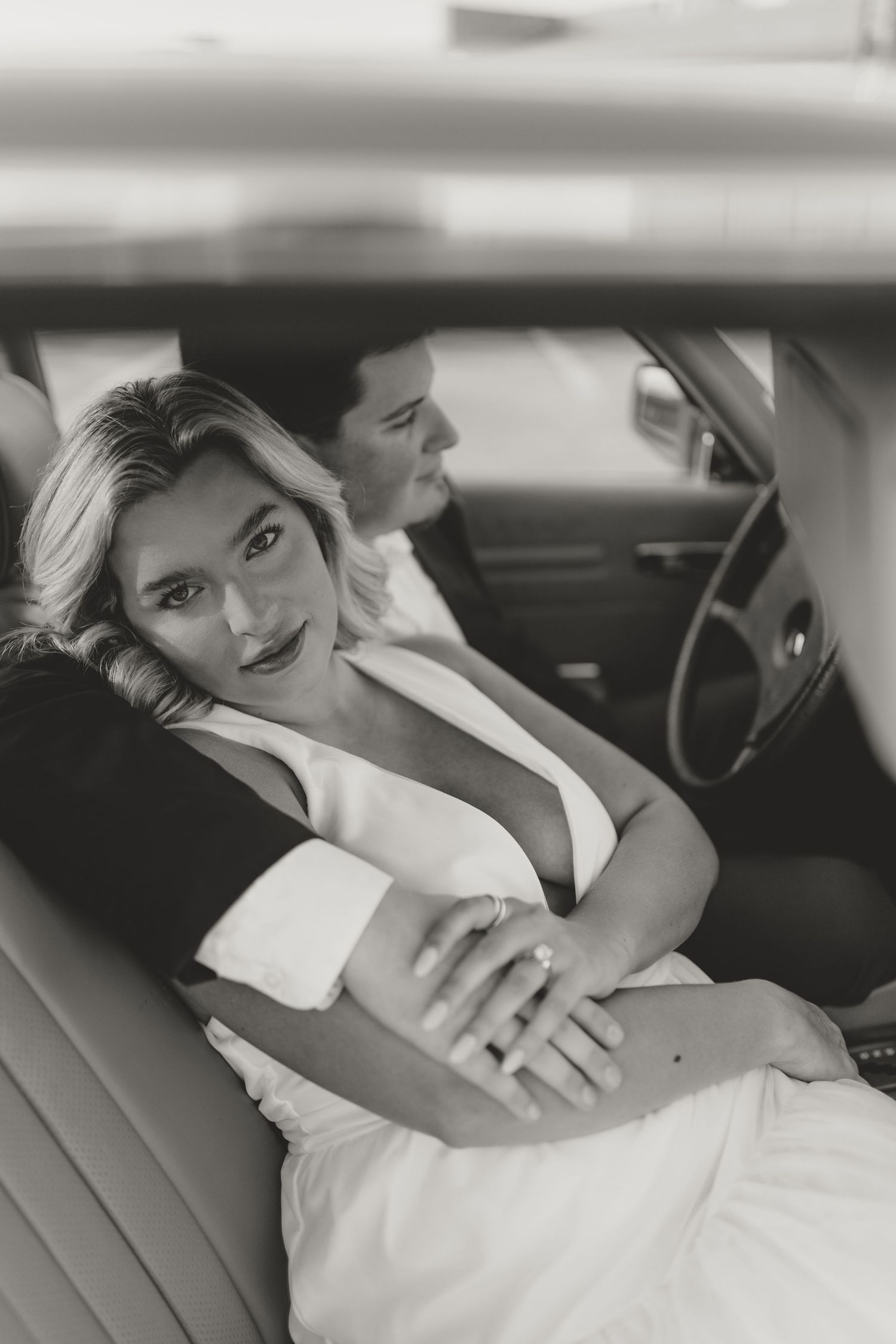 Elegant black and white portrait of a couple sitting in the backseat of a vintage car.
