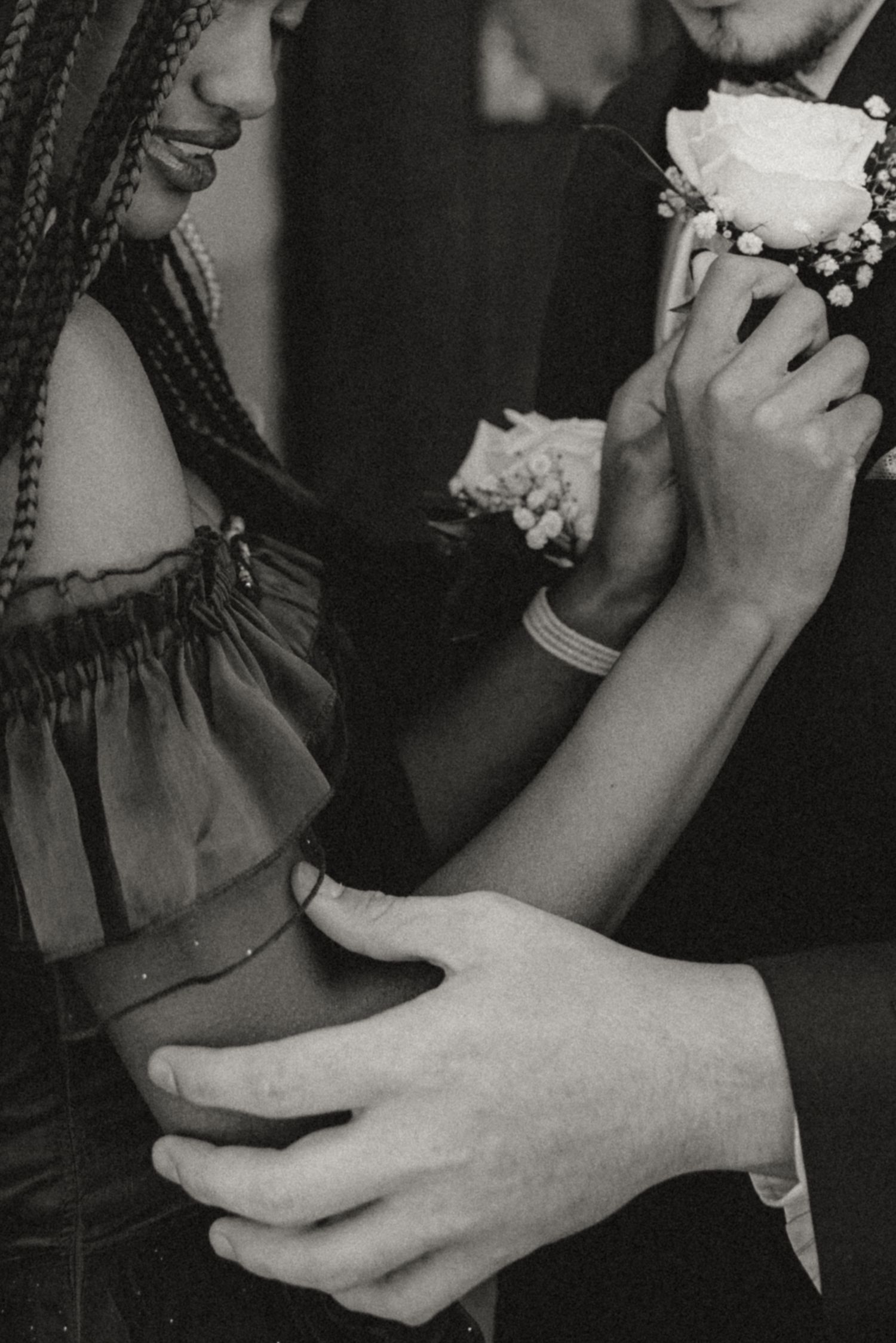 Black and white photo of a couple at prom, woman with braids wearing corsage, man in suit embracing her waist.