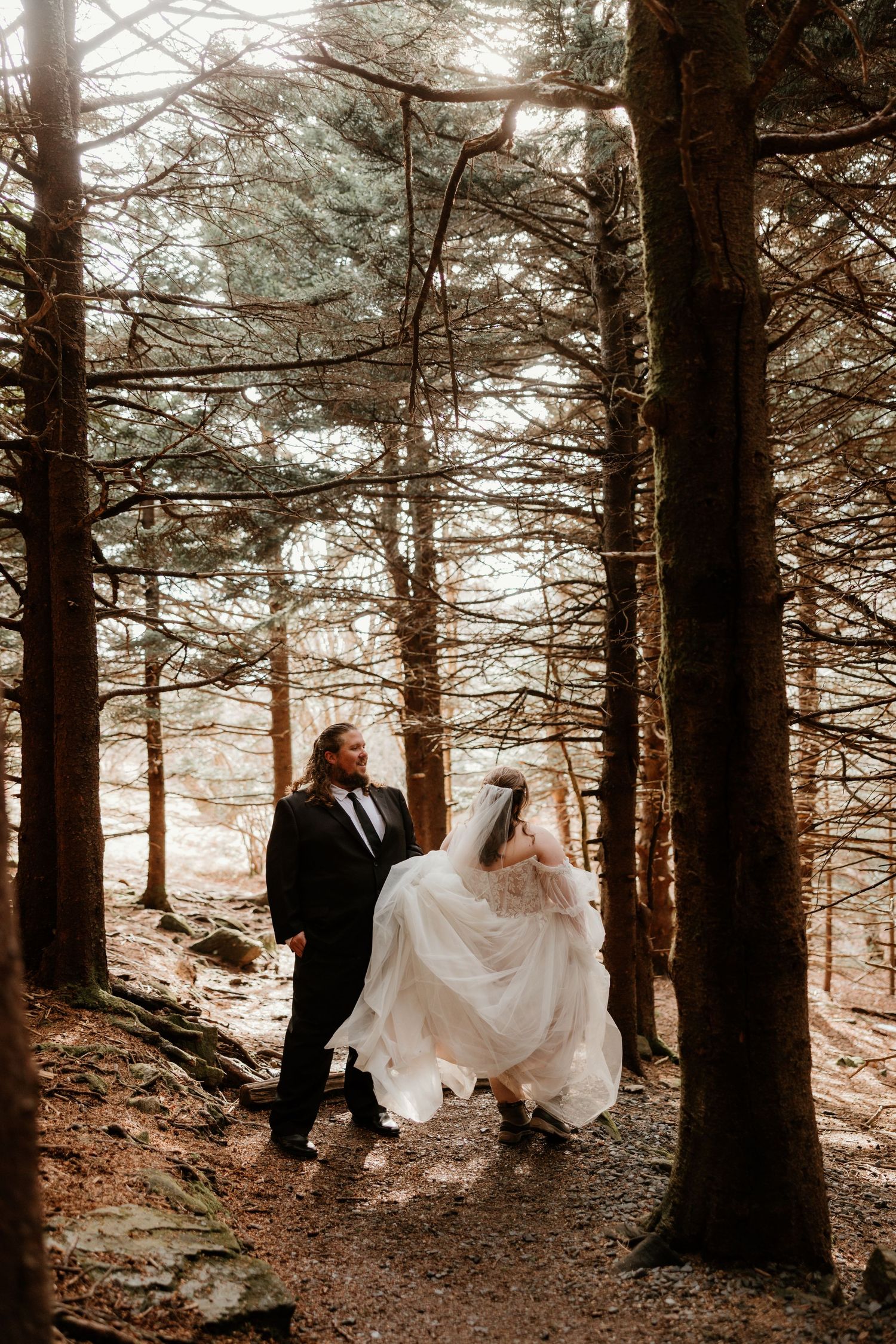 Bride and groom walking hand in hand through a sunlit forest on their wedding day.
