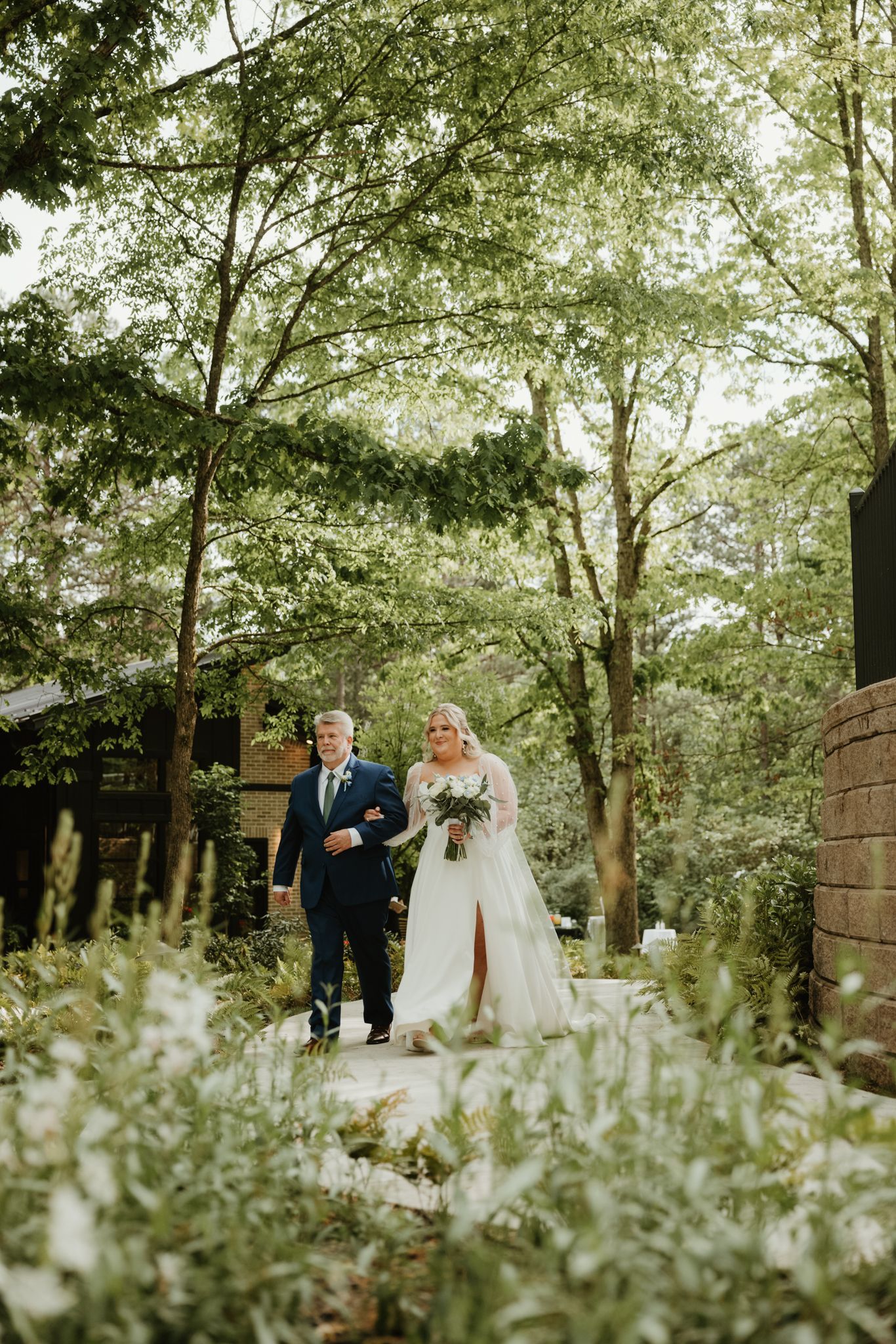 A wedding ceremony path through lush greenery with tall trees creating a natural canopy overhead.