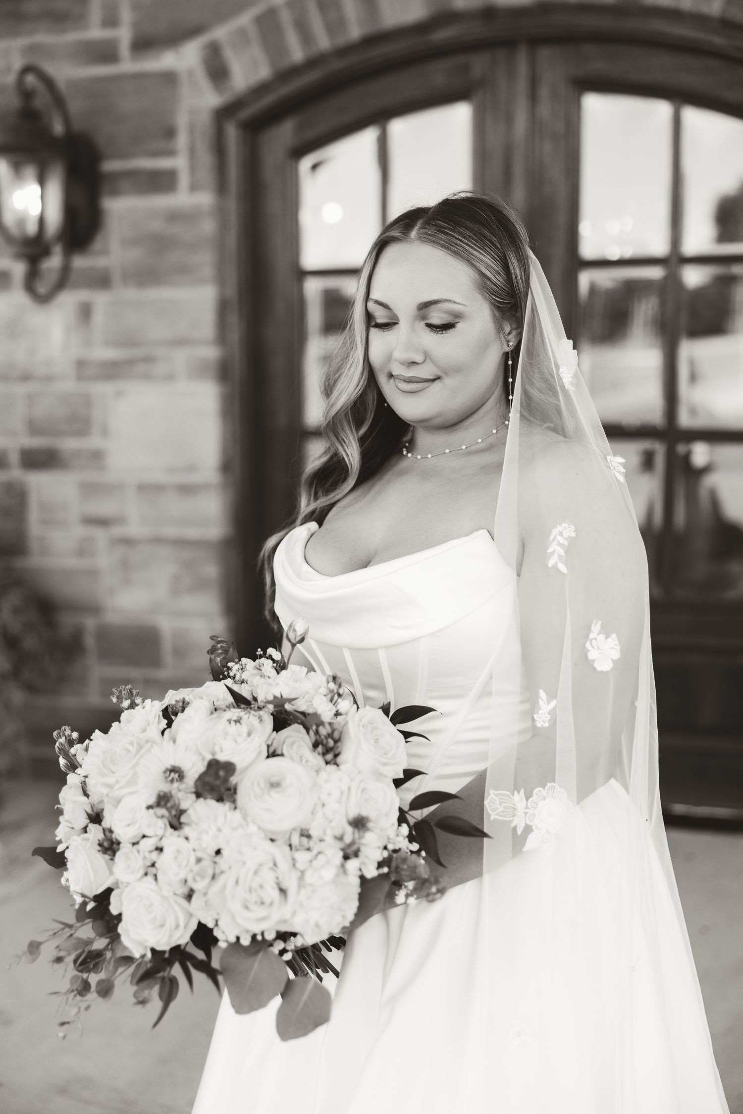 Black and white portrait of a bride in an elegant white gown holding a lush bouquet of flowers.