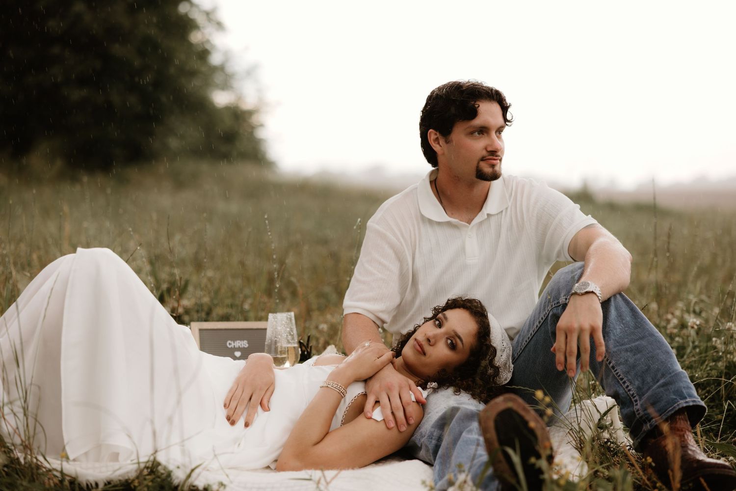 A romantic couple in white clothing laying together in a grassy field during golden hour.