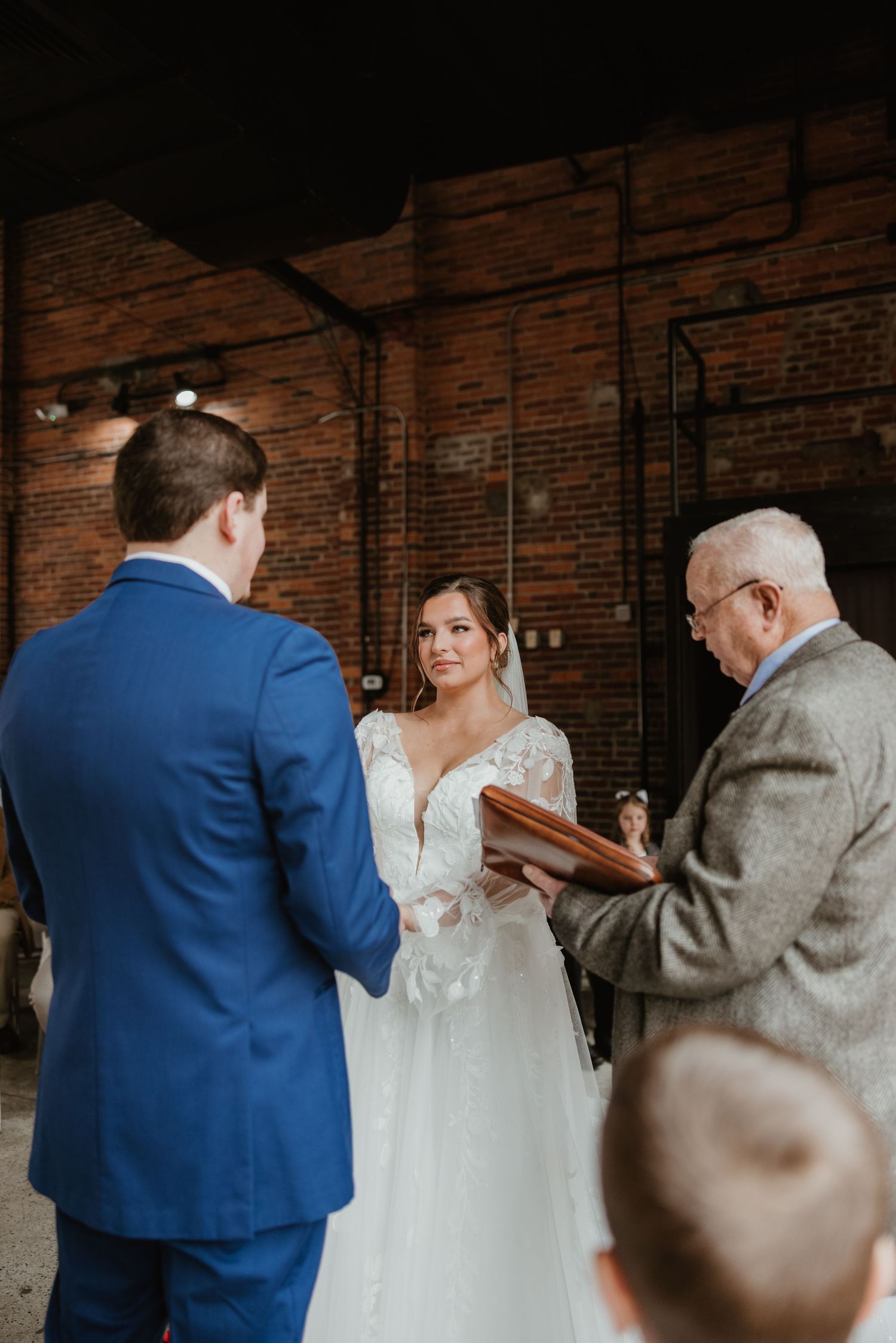 A wedding ceremony in progress inside a rustic brick-walled venue with intimate lighting.