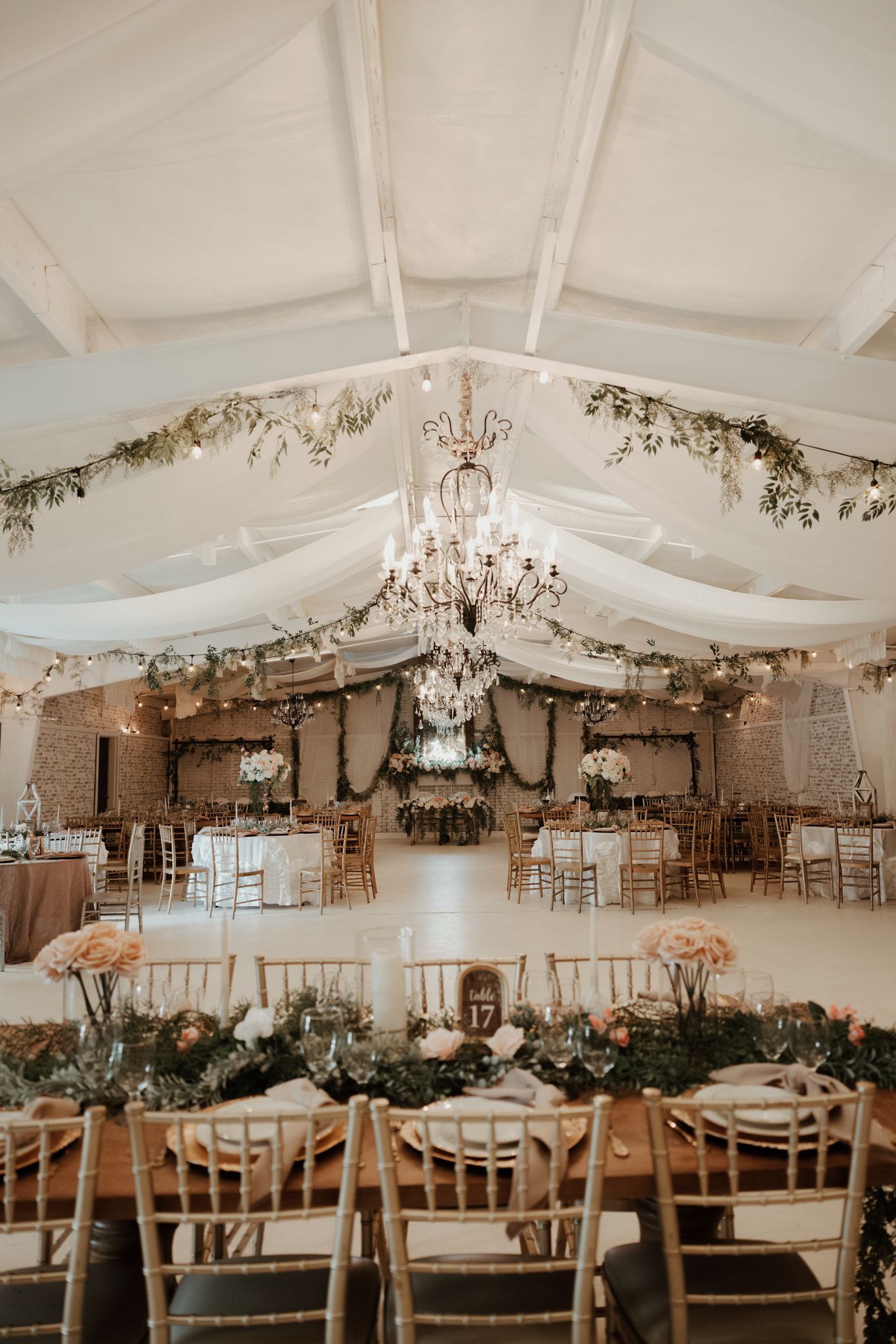 Wedding reception venue decorated with elegant white tents, crystal chandeliers, and cascading greenery for an indoor-outdoor feel.