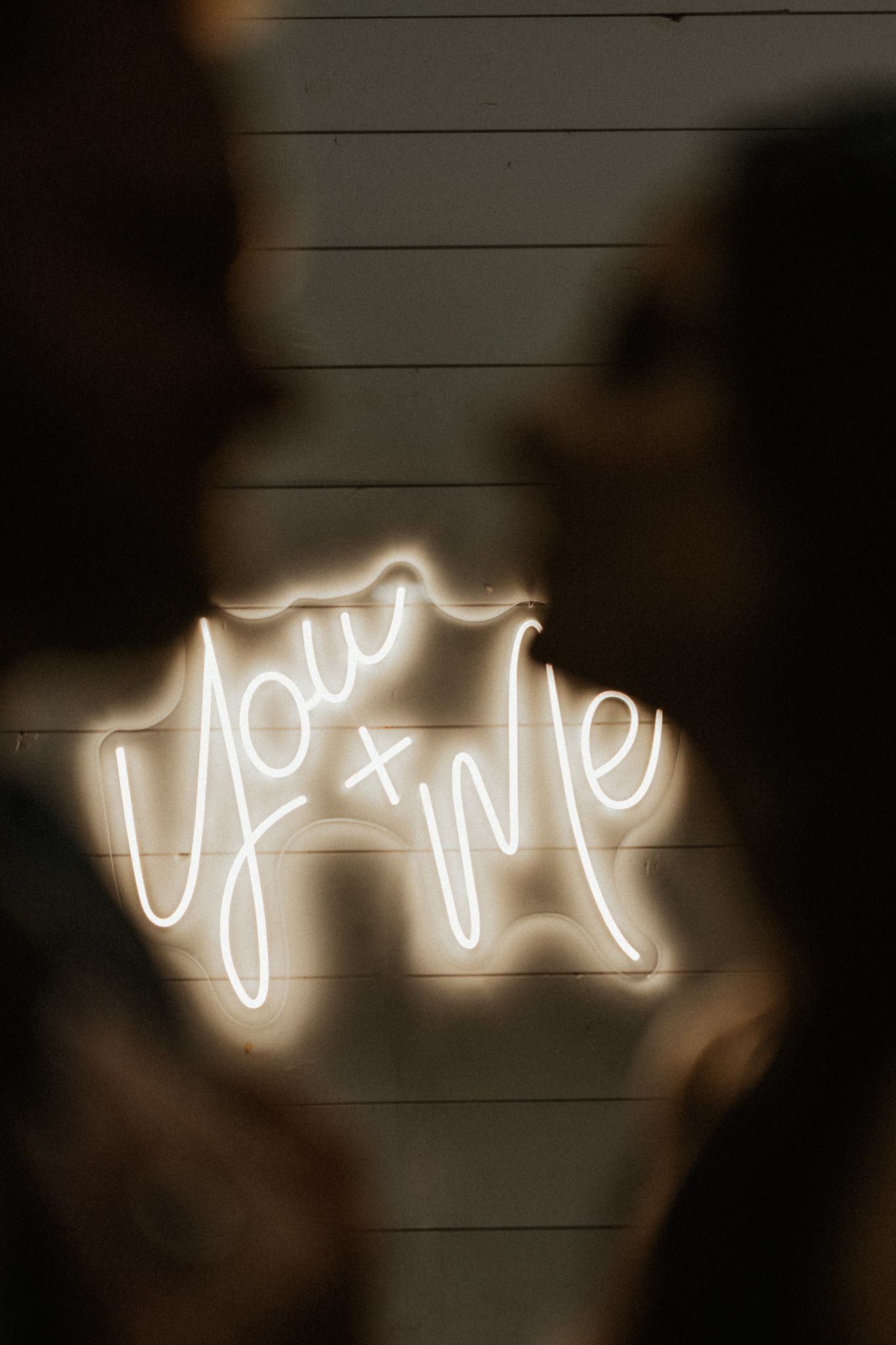 Illuminated neon cursive text glows against a dark wooden wall as wedding decor.
