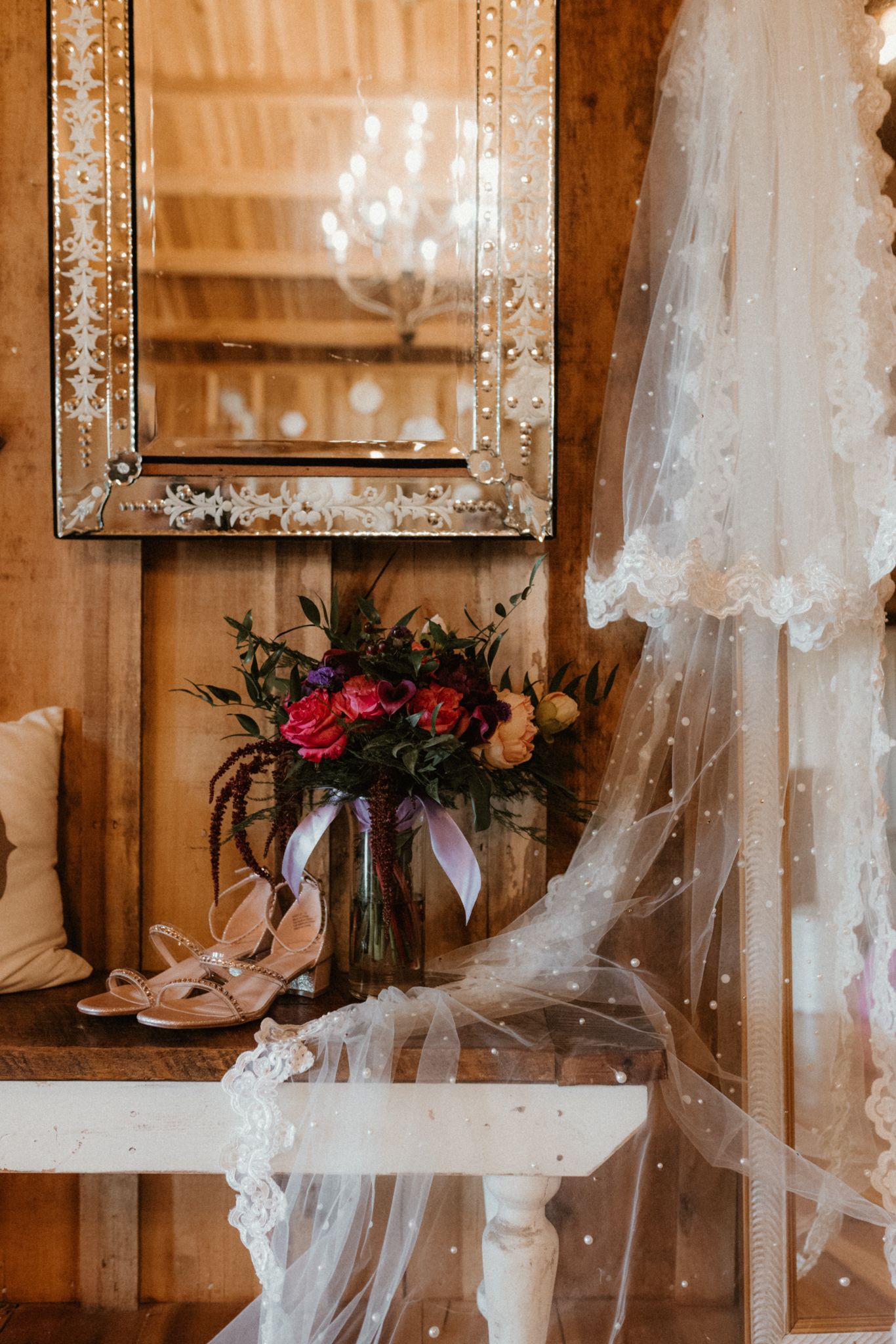 Wedding accessories including a lace veil, floral bouquet with red roses, and a framed mirror in a rustic wooden setting.