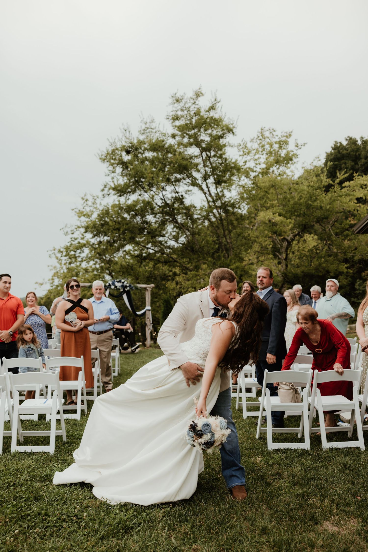 White chairs line outdoor wedding ceremony space with dramatic dip pose on grassy hill.