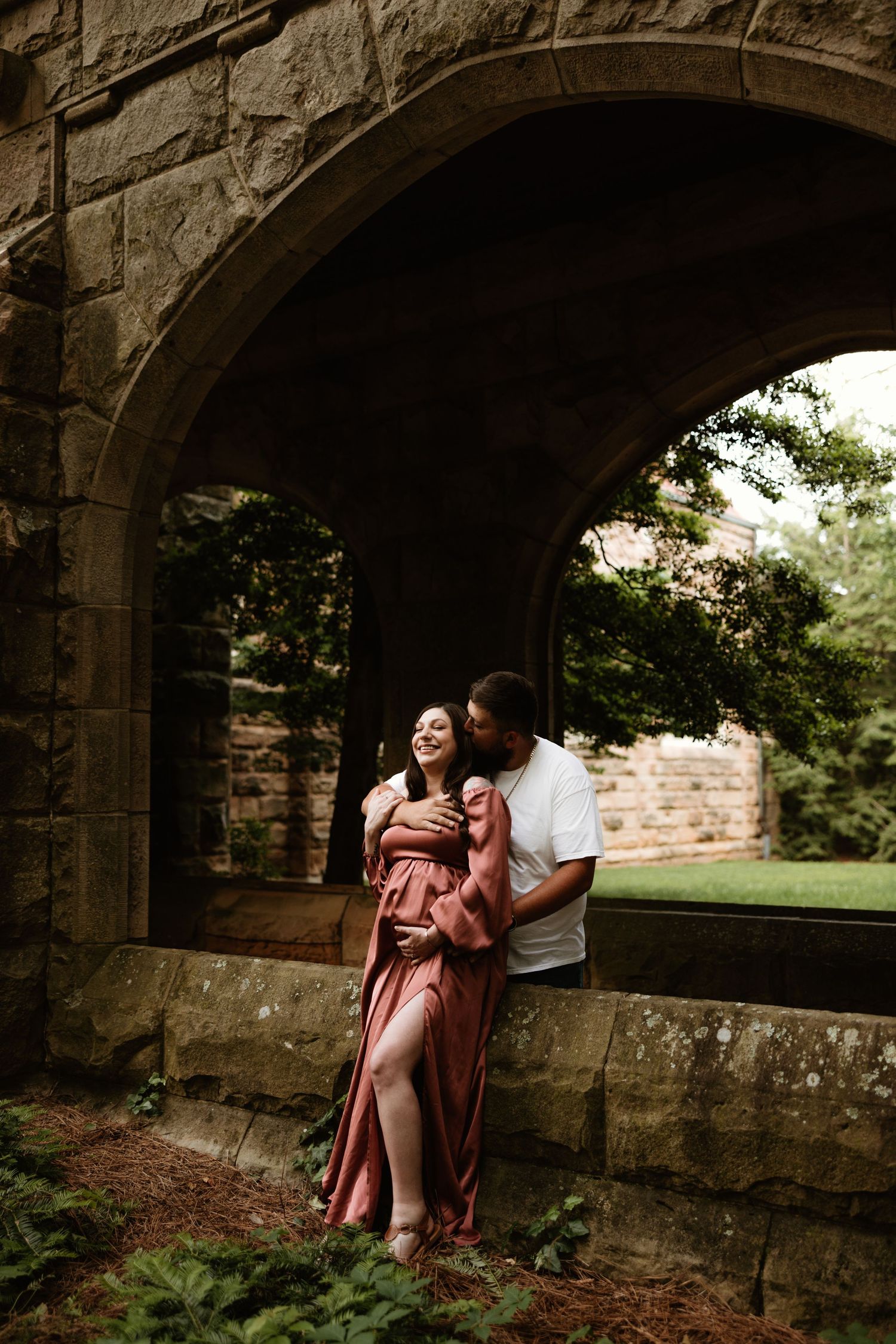 A romantic maternity photo under a stone archway in a rustic setting.