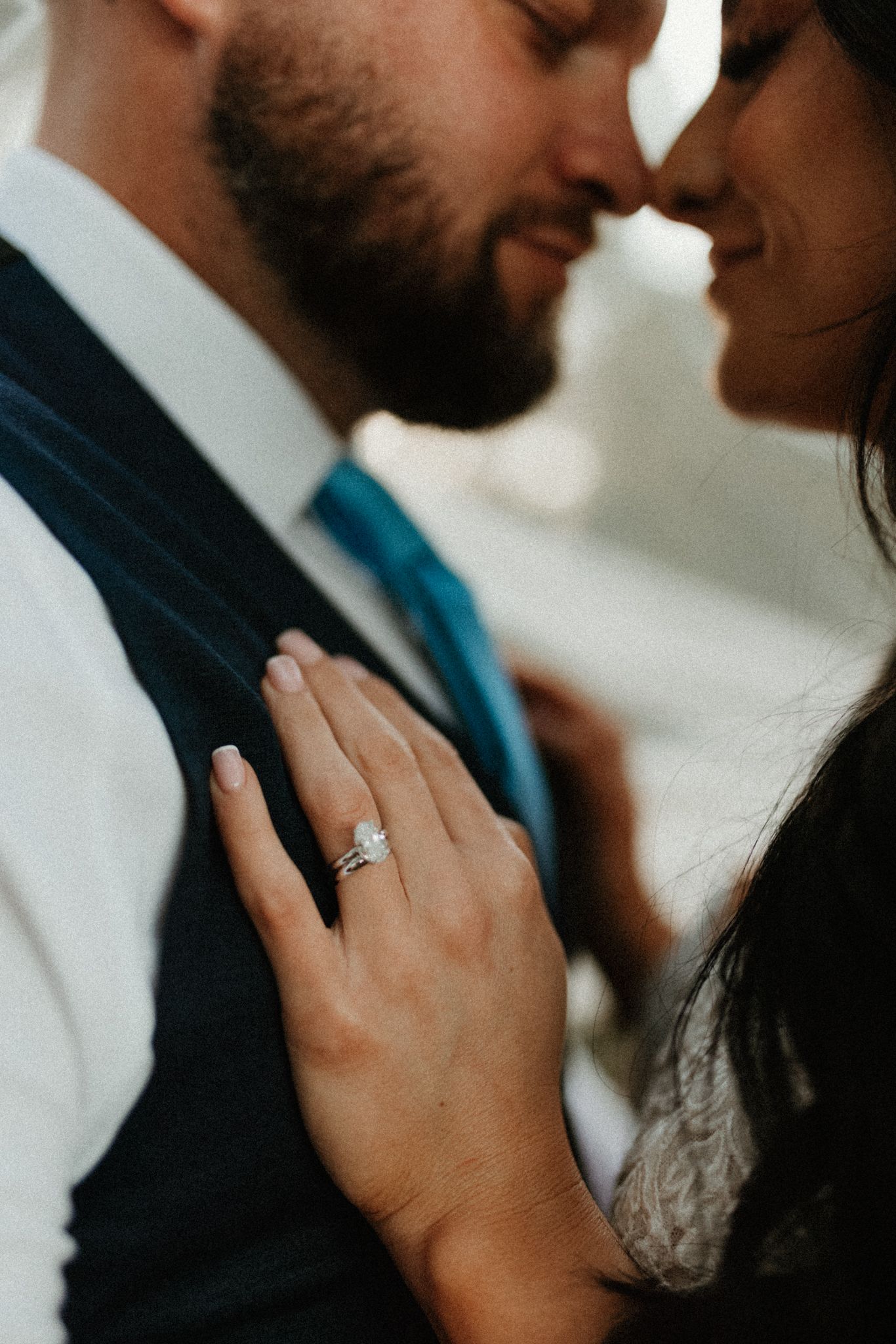 A close-up intimate moment showing an engagement ring detail as a couple embraces.