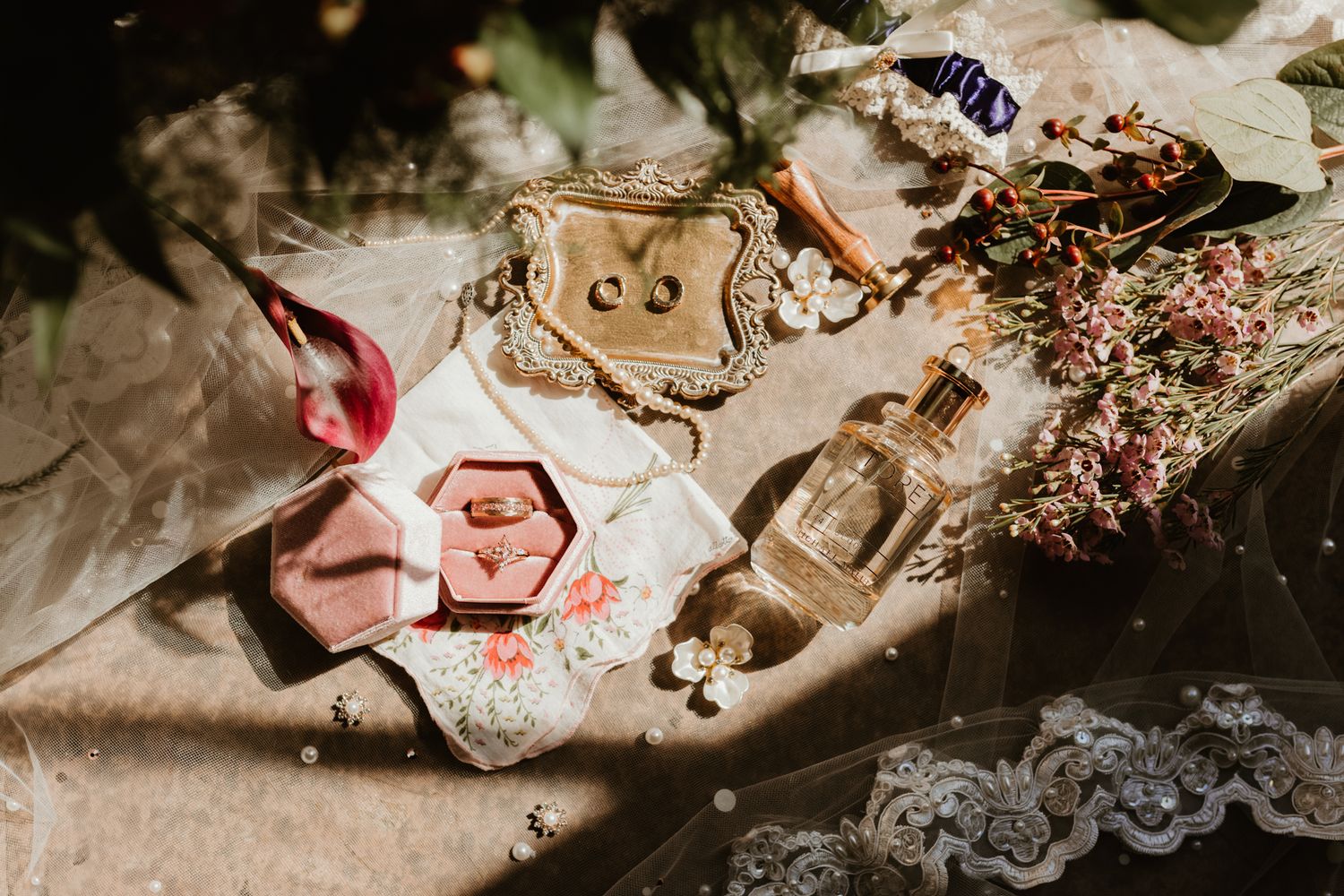 Flatlay of vintage perfume bottles, floral elements, and delicate pink paper decorations on a textured surface.