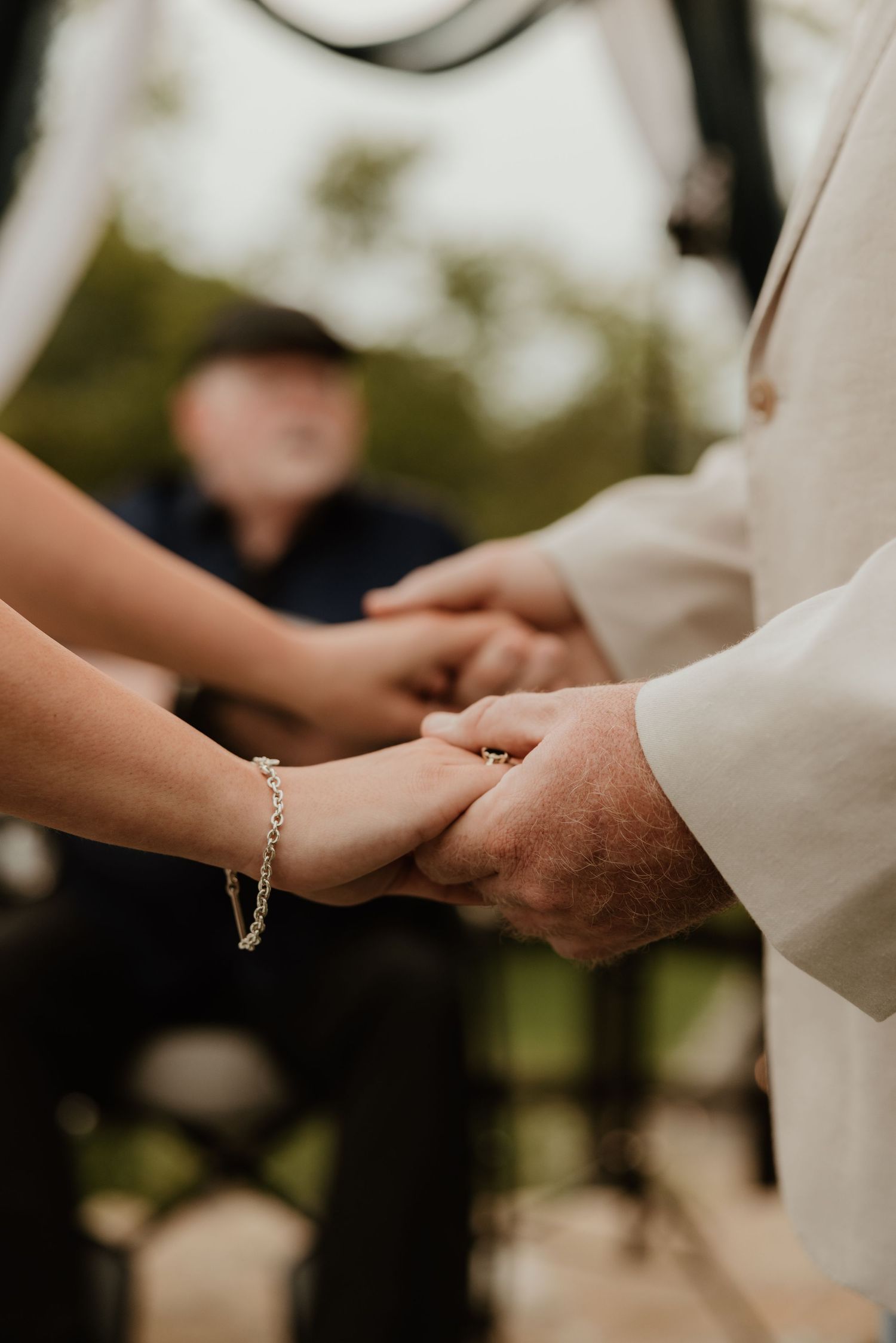 Close-up of hands exchanging rings during a tender moment at an outdoor wedding ceremony.