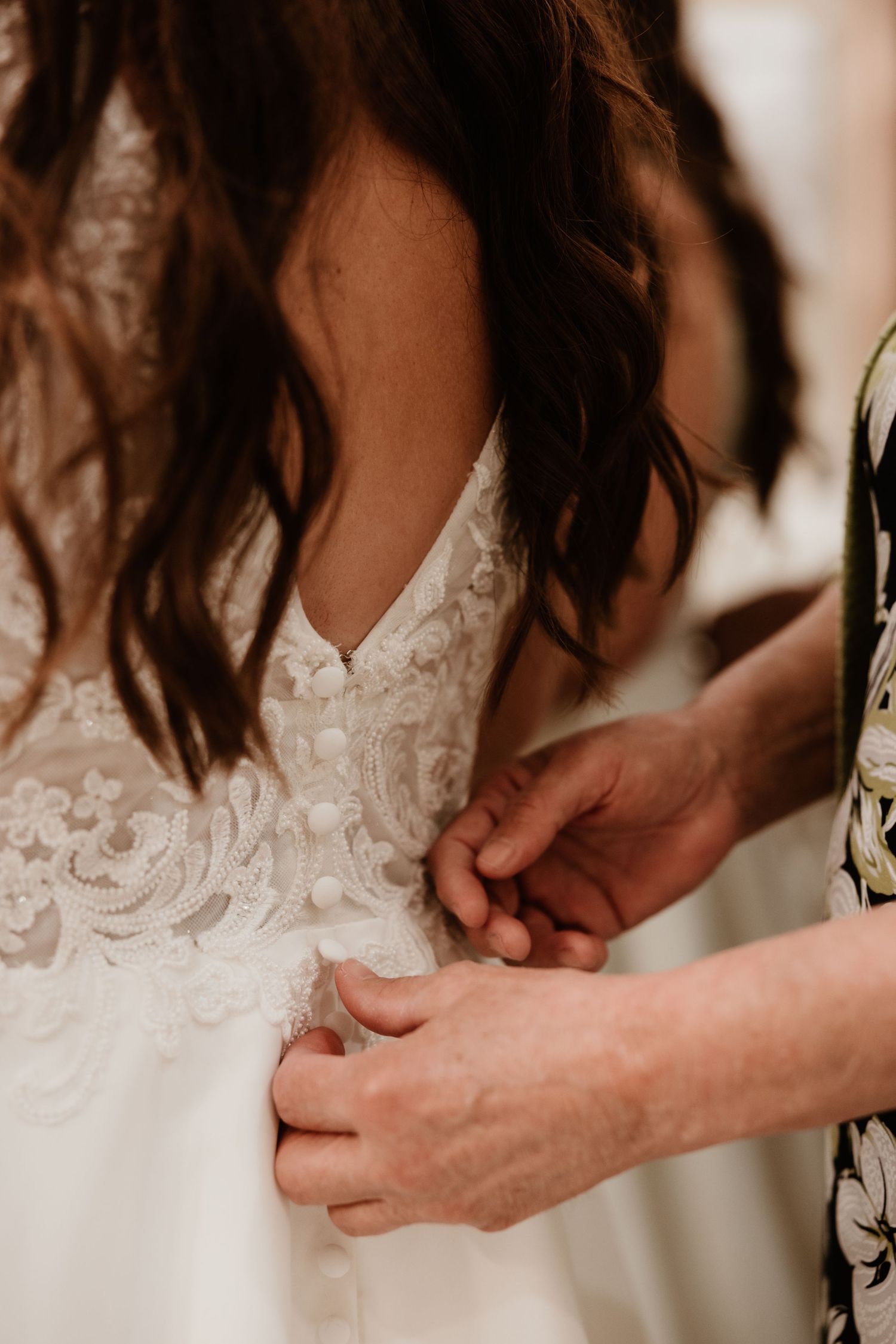 Close-up view of hands fastening buttons on a delicate white lace dress.