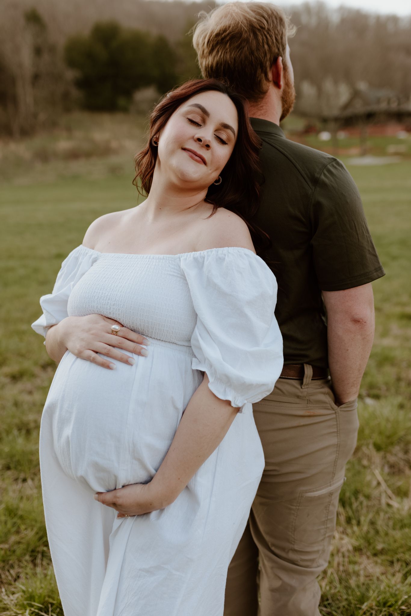 Romantic outdoor maternity photos showing couple embracing in a grassy field during golden hour.