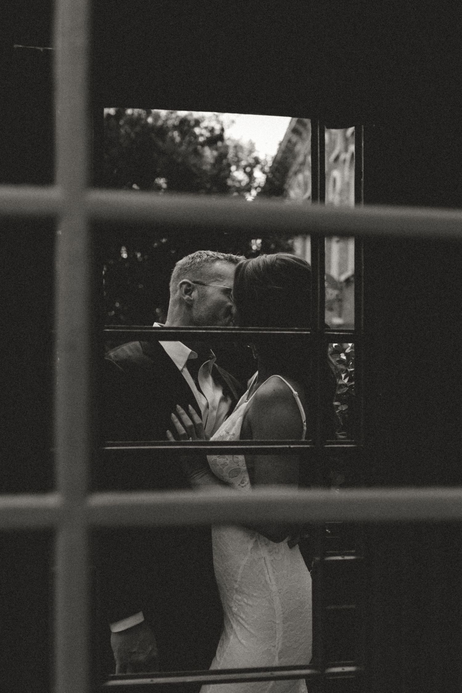 A romantic black and white photograph captured through window panes shows a couple sharing an intimate kiss.