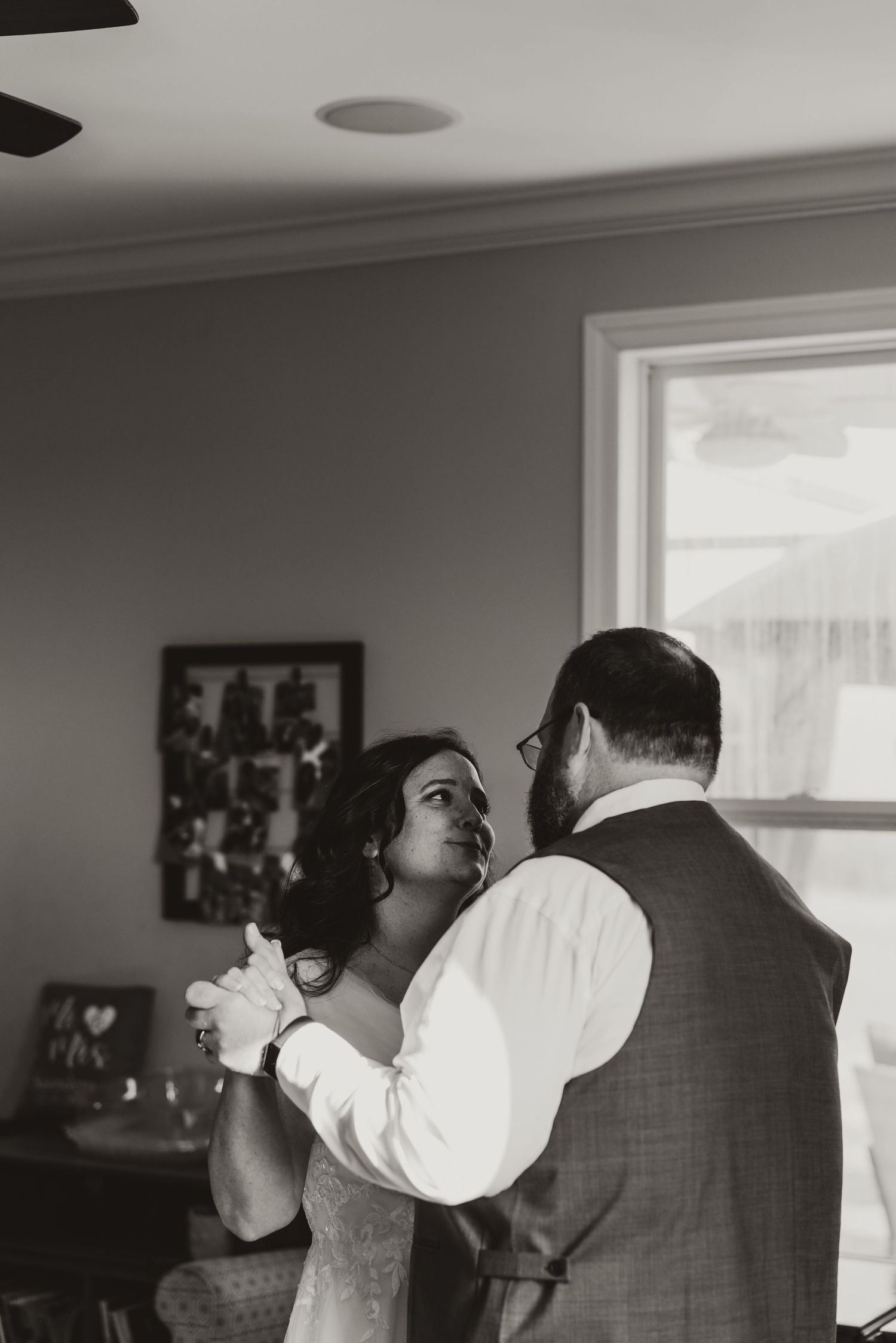 Black and white photo of a bride and groom sharing their first dance indoors near a window.