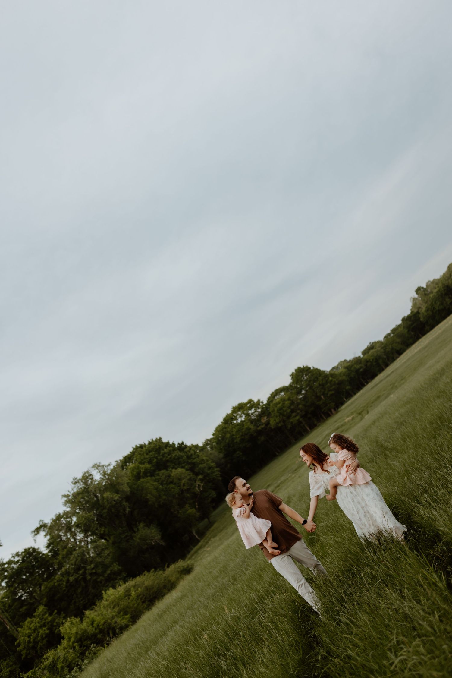 Family playing together in a lush green field with trees in the background on a cloudy day.
