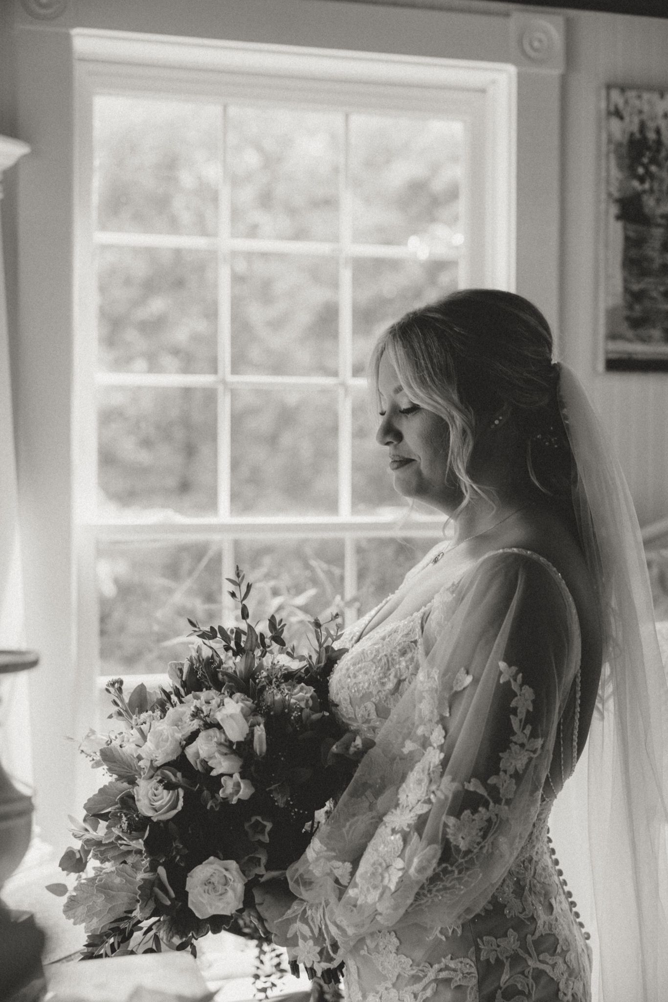 Artistic black and white bridal portrait by window with elegant bouquet.
