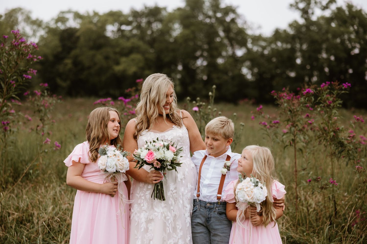 A romantic outdoor wedding party poses in a field of wildflowers wearing pink dresses and gray suits.