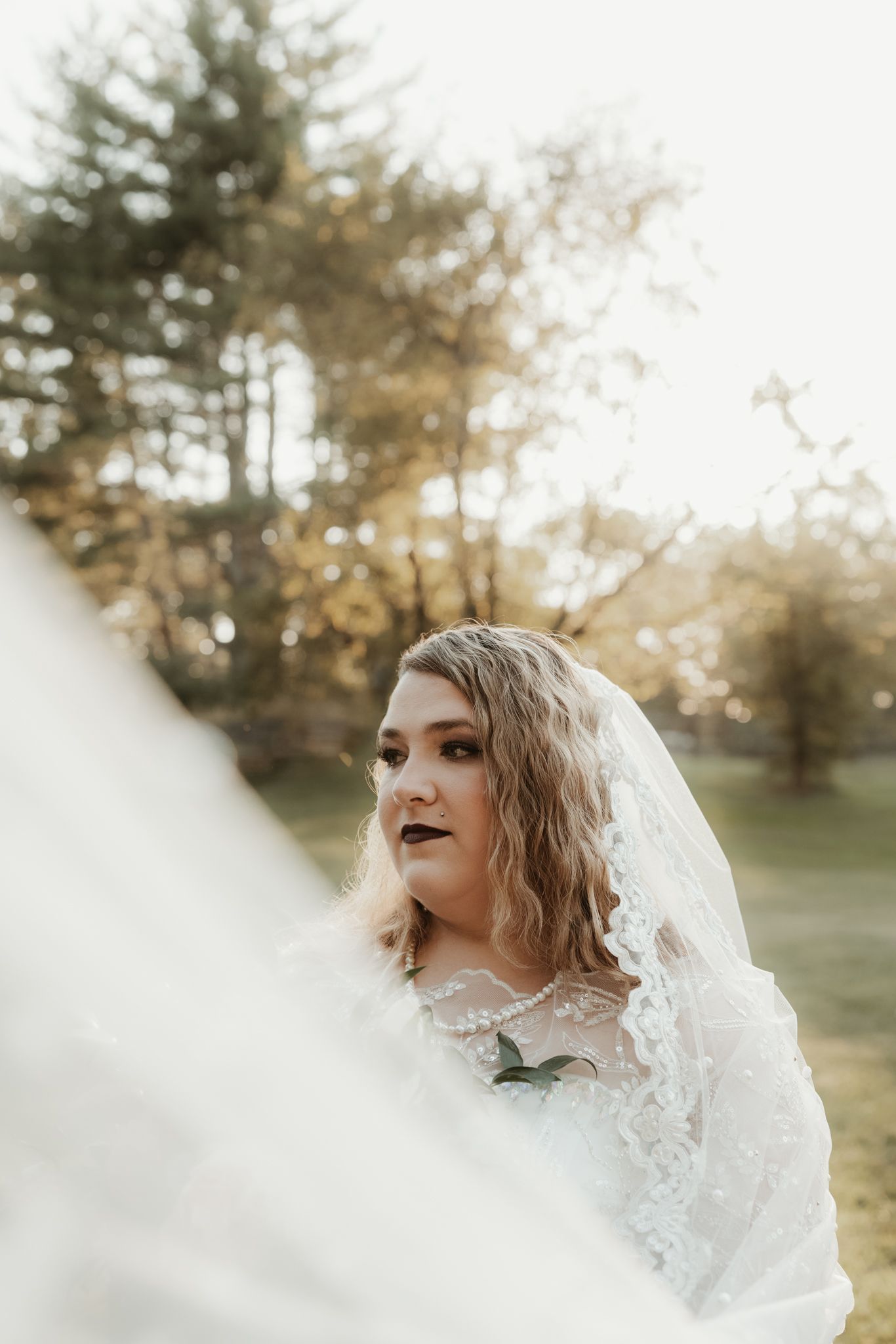 Ethereal bridal portrait with soft lighting and delicate lace veil against a dreamy natural backdrop.