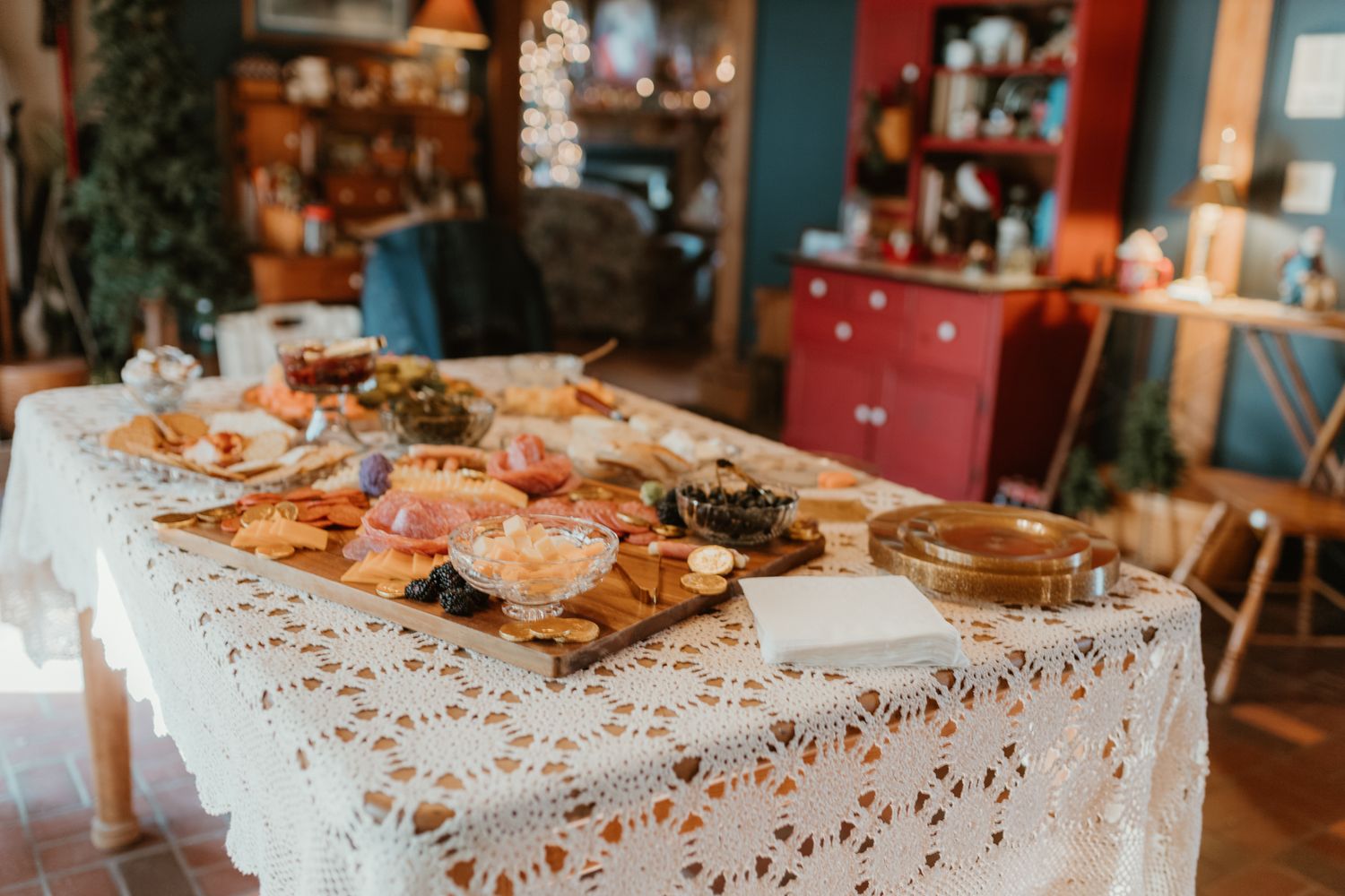 Various pastries and baked goods displayed on a lace tablecloth in a cozy rustic dining room setting.
