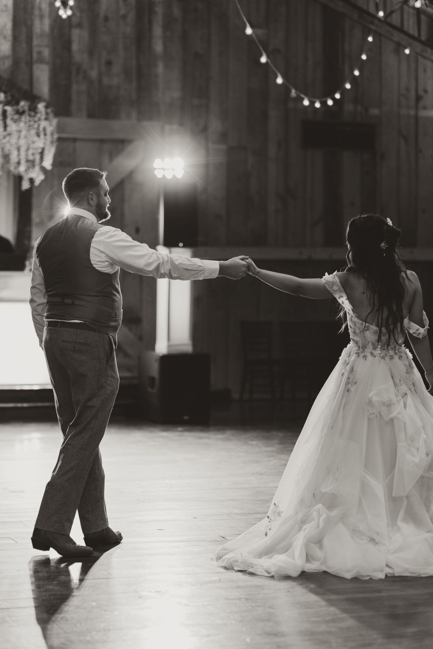 Black and white wedding dance photos under twinkling string lights in a rustic venue.
