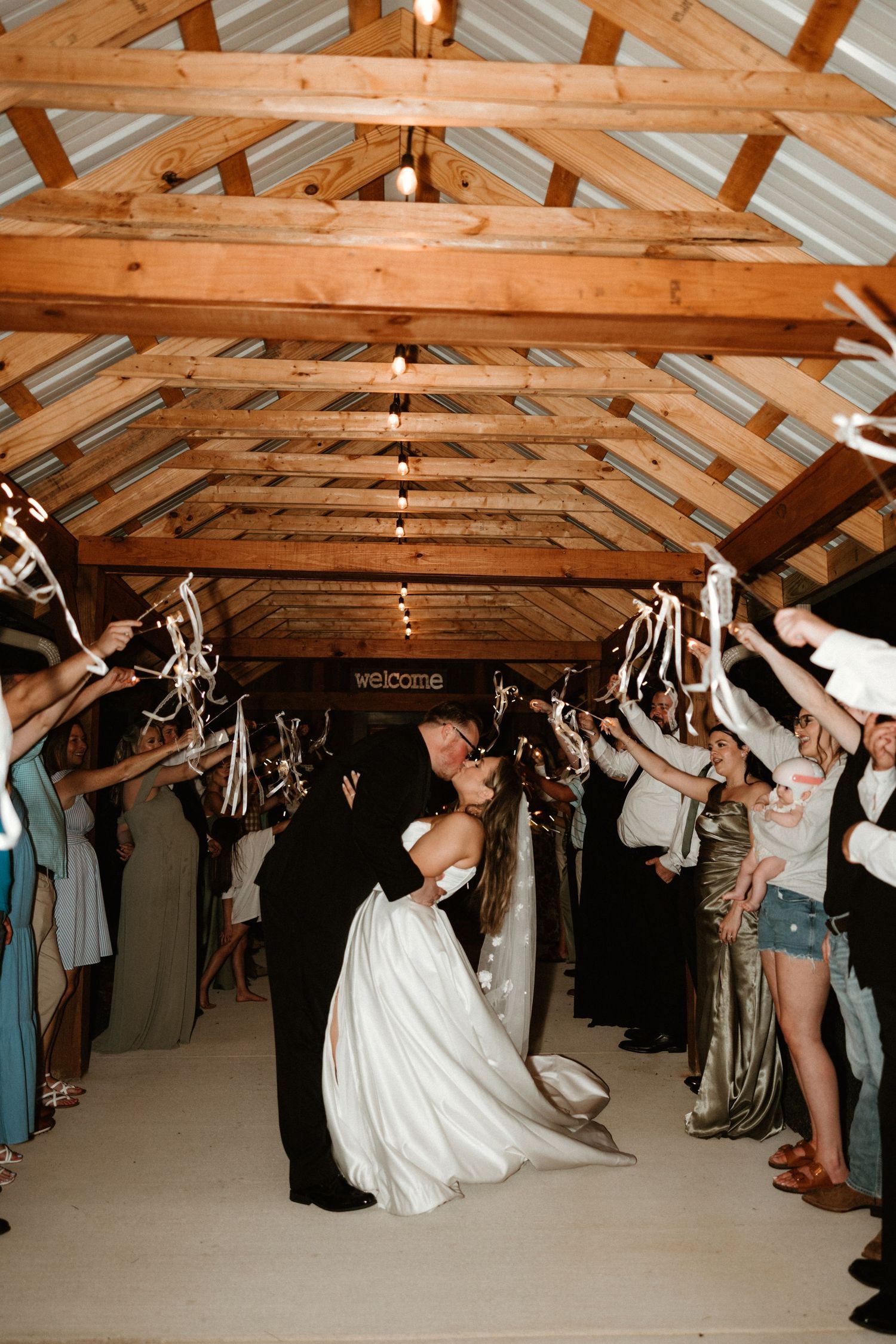 Sequence of photos showing wedding reception guests lined up under wooden beams doing a fun group dance in rustic venue.