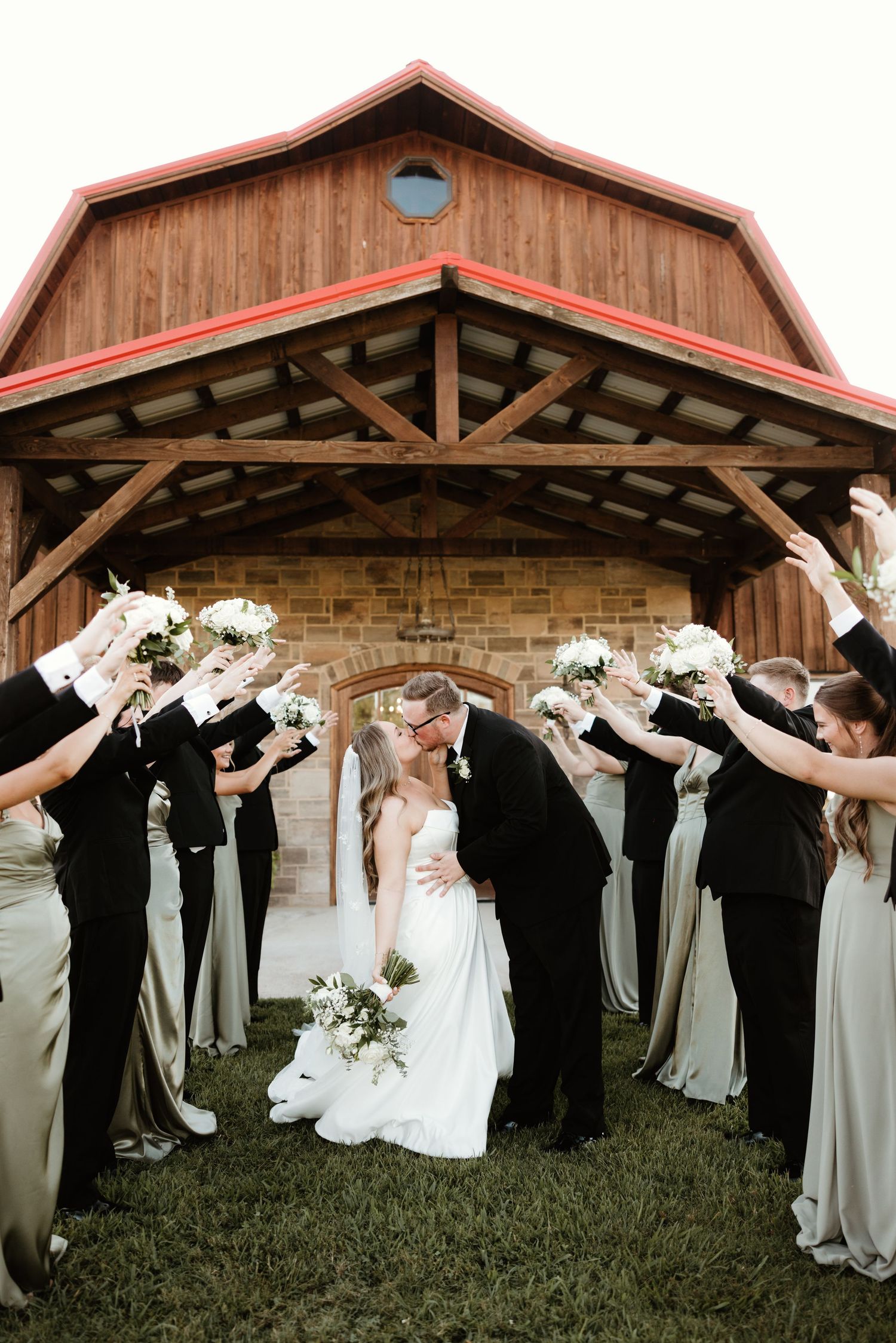 Wedding party poses in a sequence showing them all bowing forward together in front of a rustic wooden barn.