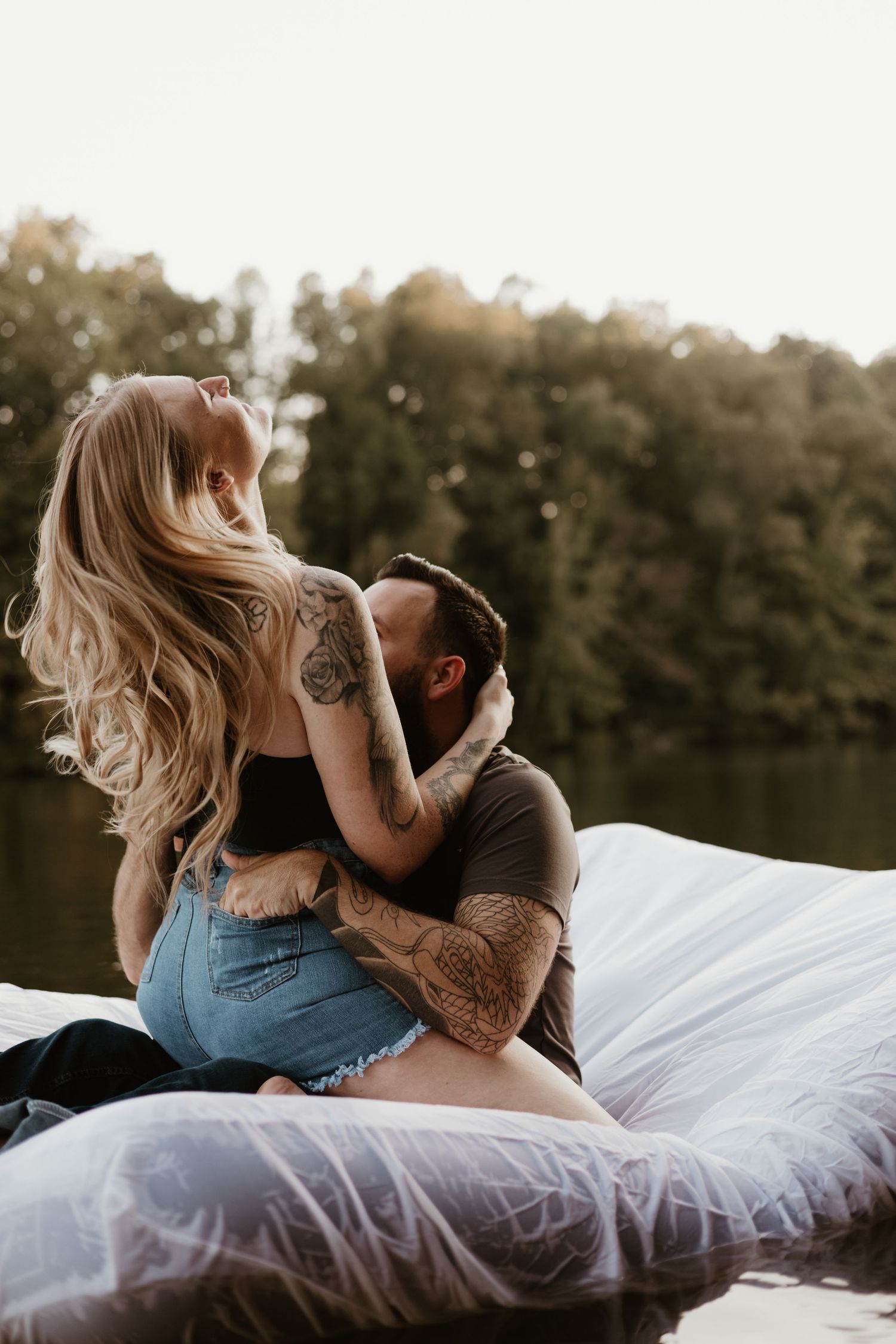 Intimate couple photoshoot on white bedding with natural lighting.